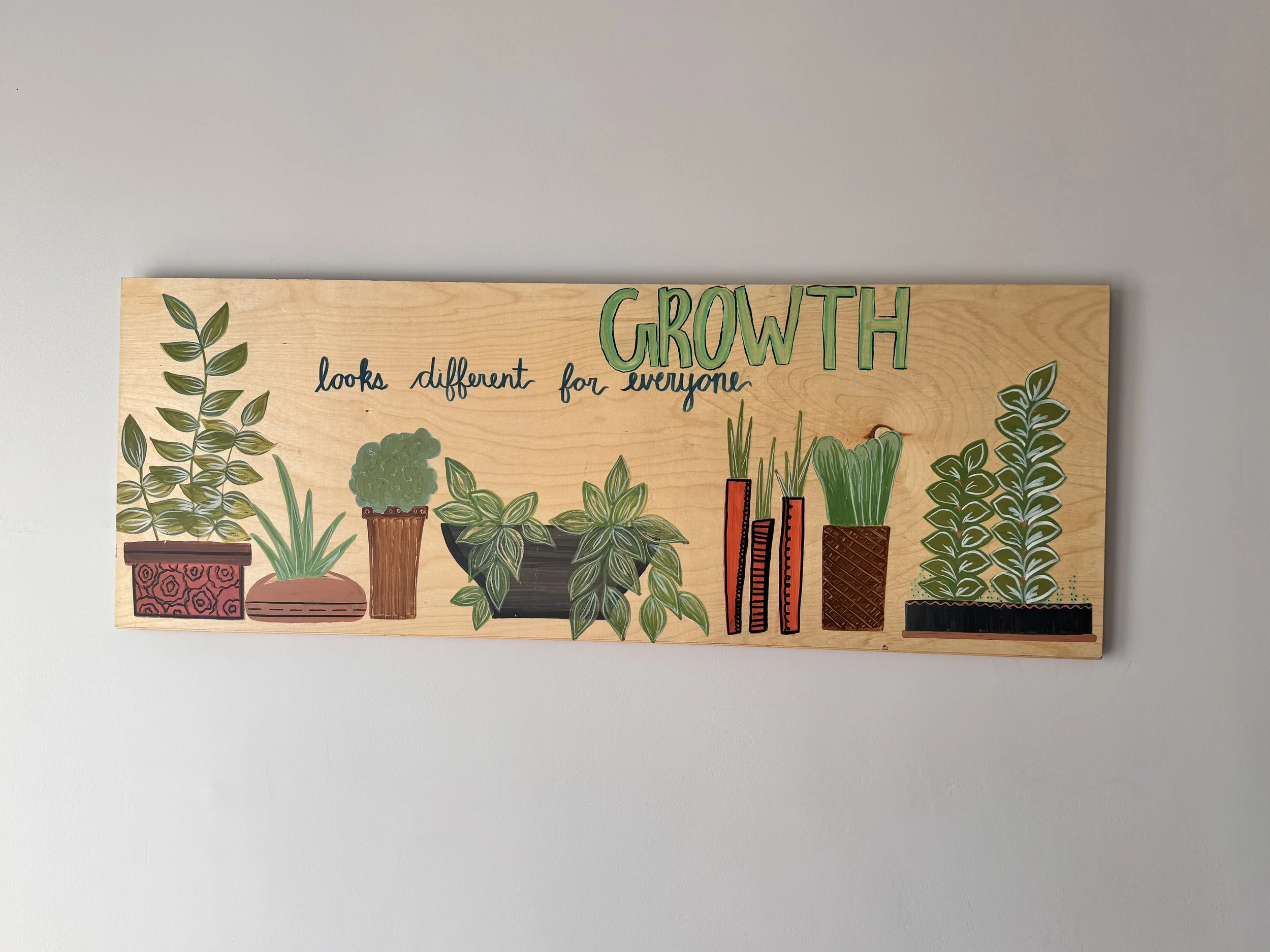 Hand-painted wooden sign with green plants in pots and text reading 'Growth looks different for everyone'