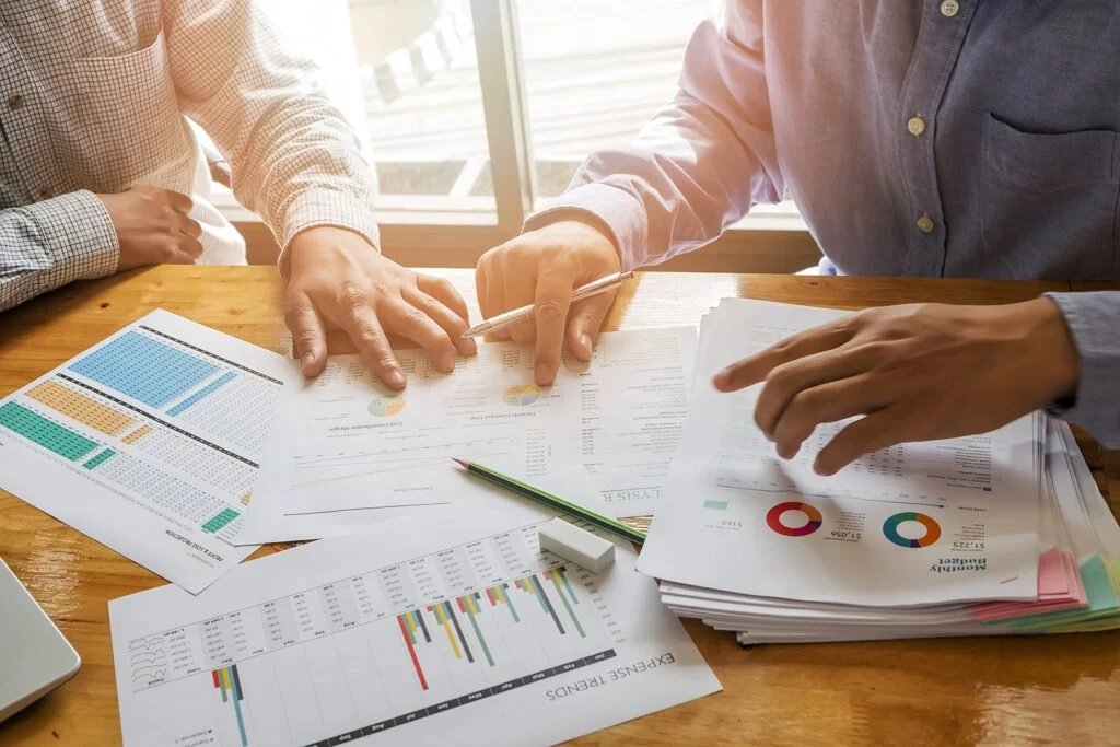 Two individuals reviewing financial graphs and charts on a wooden table.