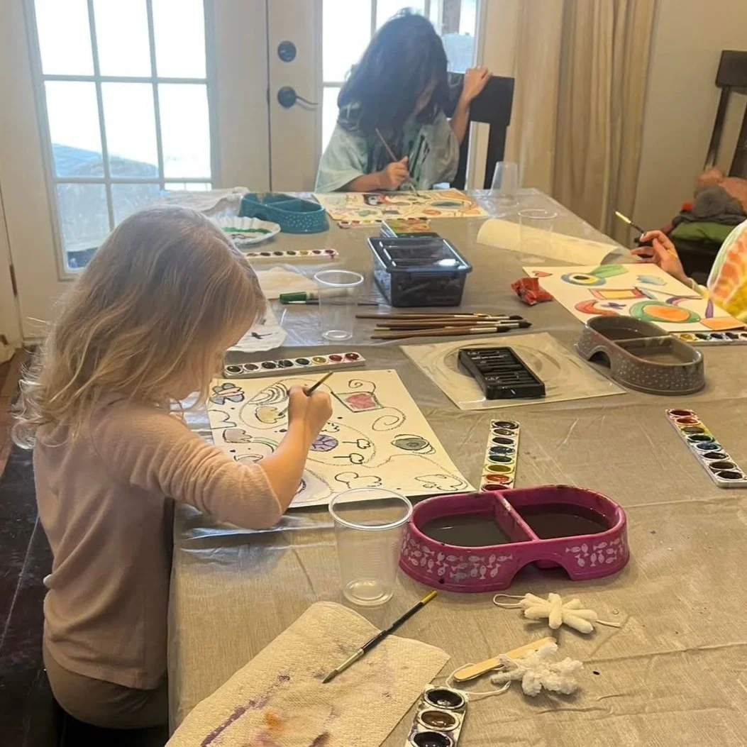 Children painting at a table with watercolor paints and brushes.