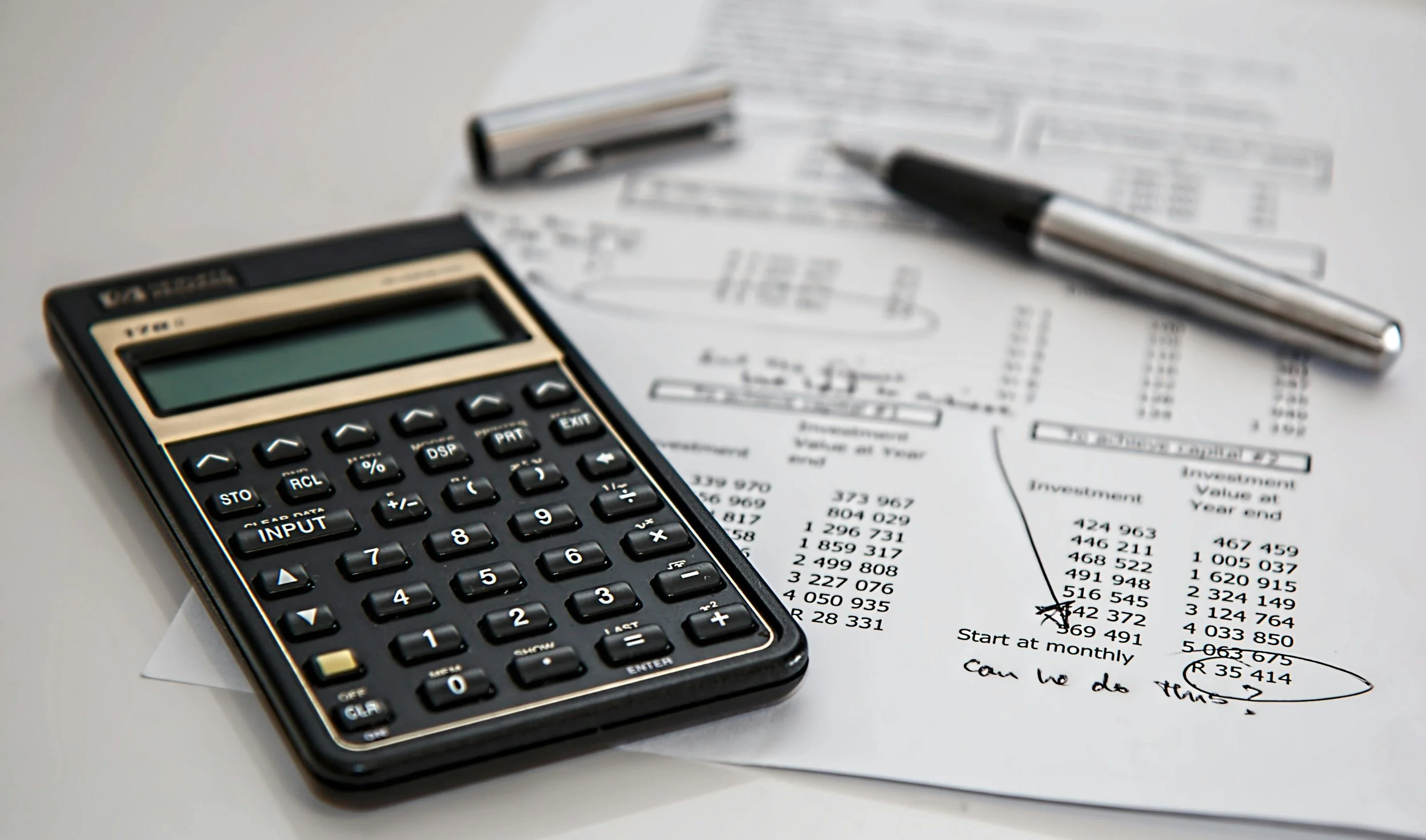 Calculator, pen, and financial documents with handwritten notes and calculations on a white surface.