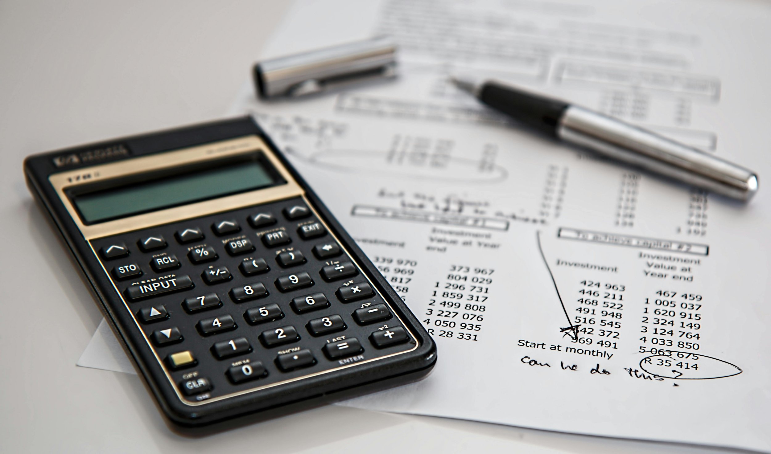 Calculator, pen, and financial documents with handwritten notes and marked cash figures on a white surface.