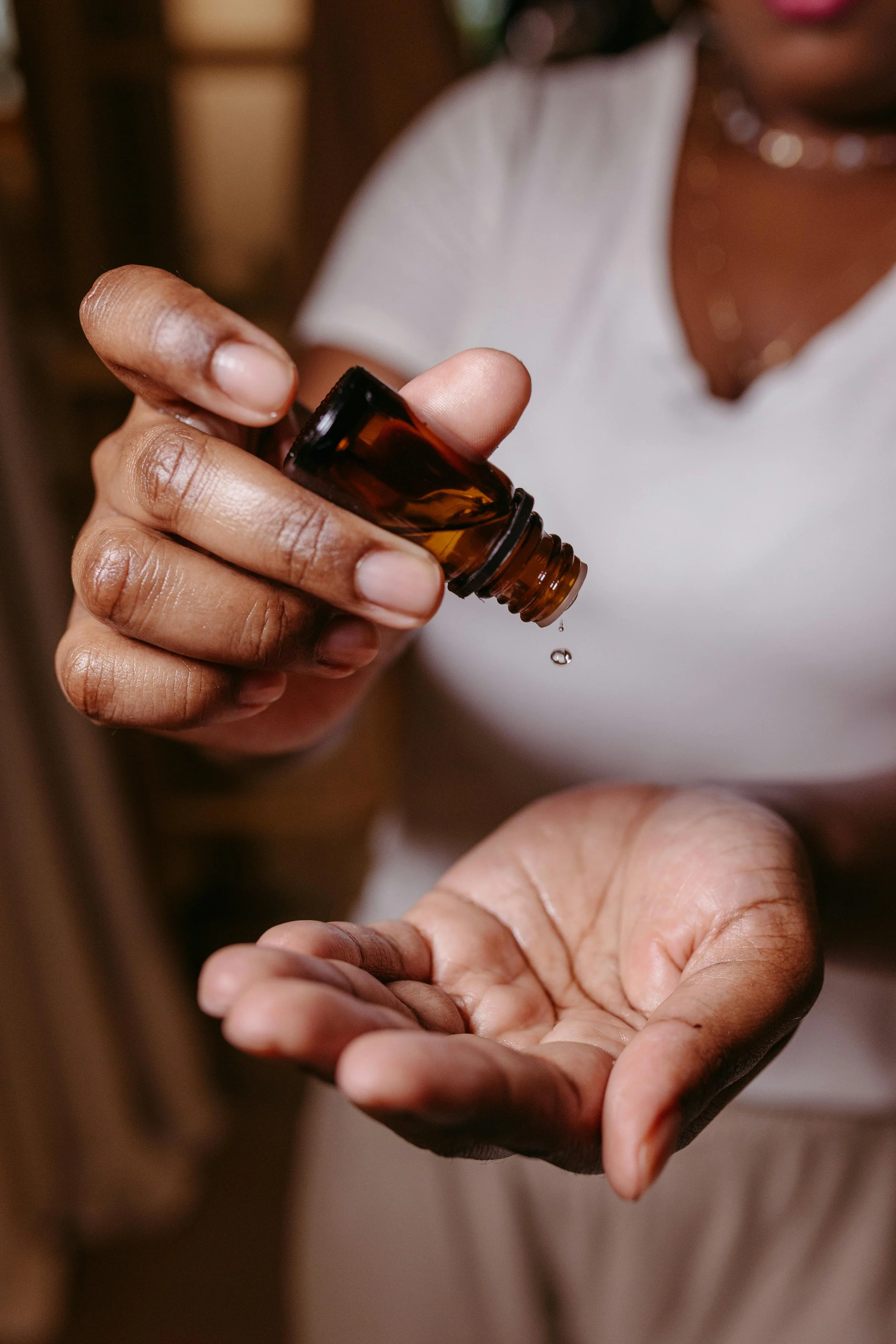 A person pouring liquid medicine or essential oil from a brown glass bottle into their open palm.
