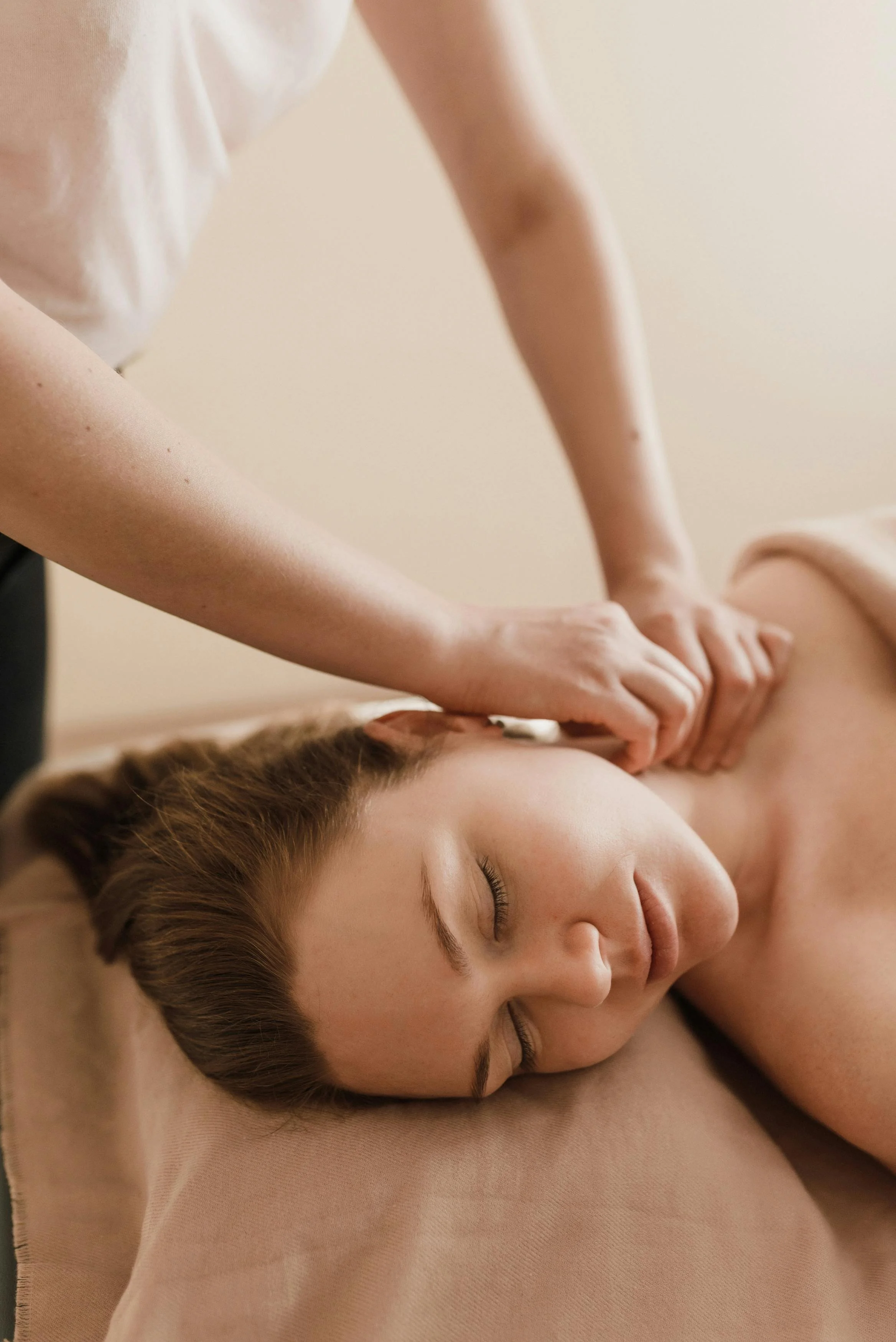 A woman receiving a massage while lying on a massage table with her eyes closed.