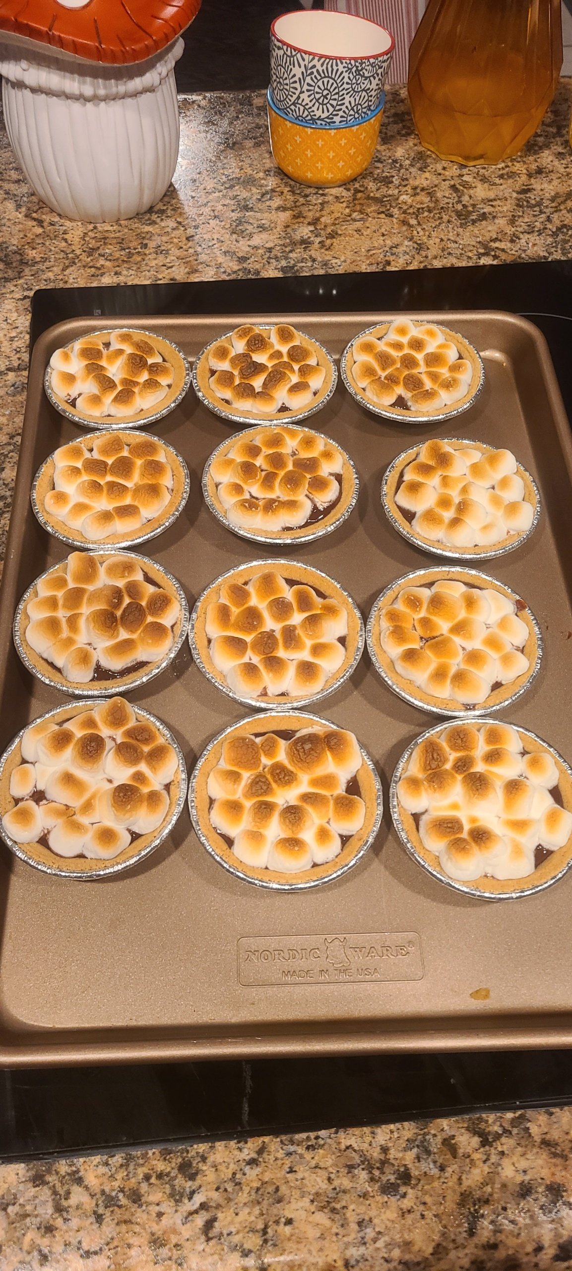 Baked mini pies with toasted marshmallow topping on a baking sheet, granite countertop