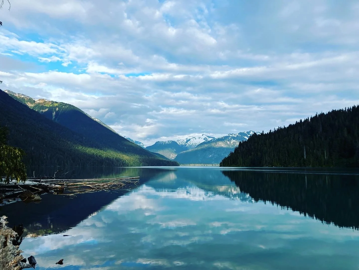 Calm lake with reflection of mountains and trees, under a partly cloudy sky.