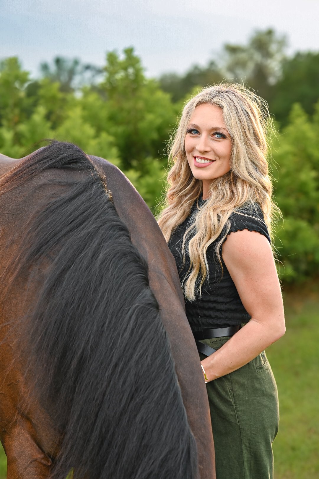 A woman with long blonde hair standing next to a horse outdoors.
