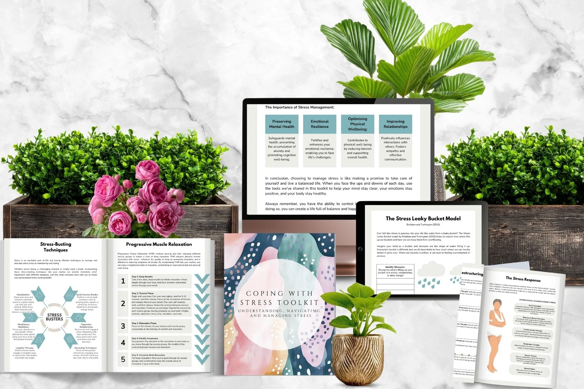 An arrangement of wellness and stress management materials on a white marble surface, including a book titled 'Coping with Stress Toolkit,' several printed sheets with stress techniques and bucket models, two potted plants, pink flowers, and two electronic tablets displaying informational content.