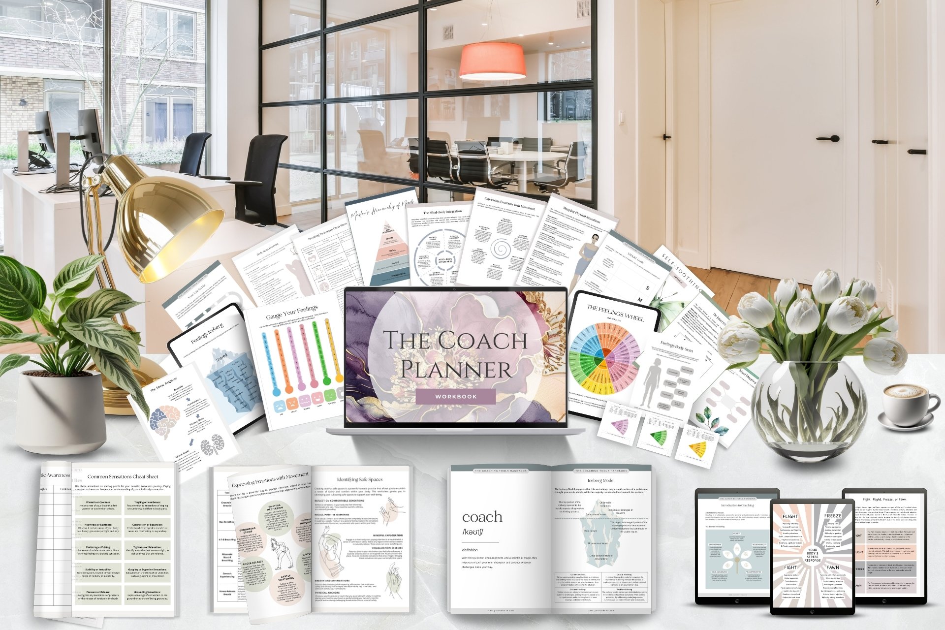 A desk setup with various printed coaching materials, a laptop displaying 'The Coach Planner' workbook, potted plants, a gold desk lamp, and a vase of white tulips in an office with glass walls.