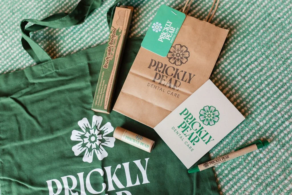 An image depicting many of the sustainability-minded items that we give to new patients or sell at our office, including an organic cotton tote bag, a bamboo toothbrush, plastic-free lip balm, and more.