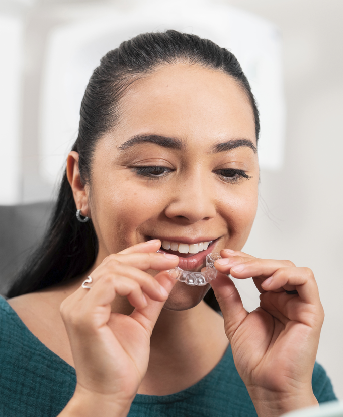 An image of a seated woman placing a ClearCorrect clear aligner into her mouth, illustrating the sort of clear-aligner technology offered by Dr. Flores at Prickly Pear Dental Care.