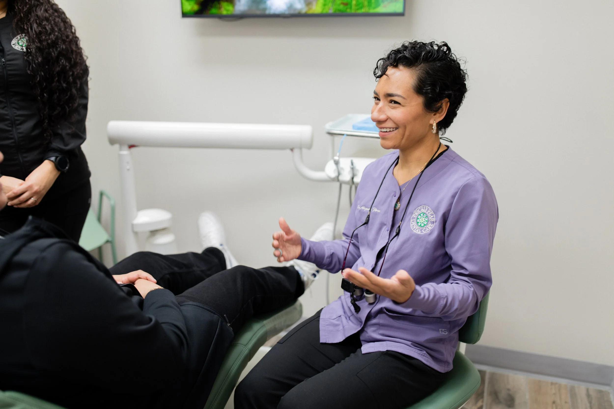 An image of Dr. Alejandra Flores Arellano, the owner and dentist here at Prickly Pear Dental Care, explaining a topic to a patient seated in a dental chair.