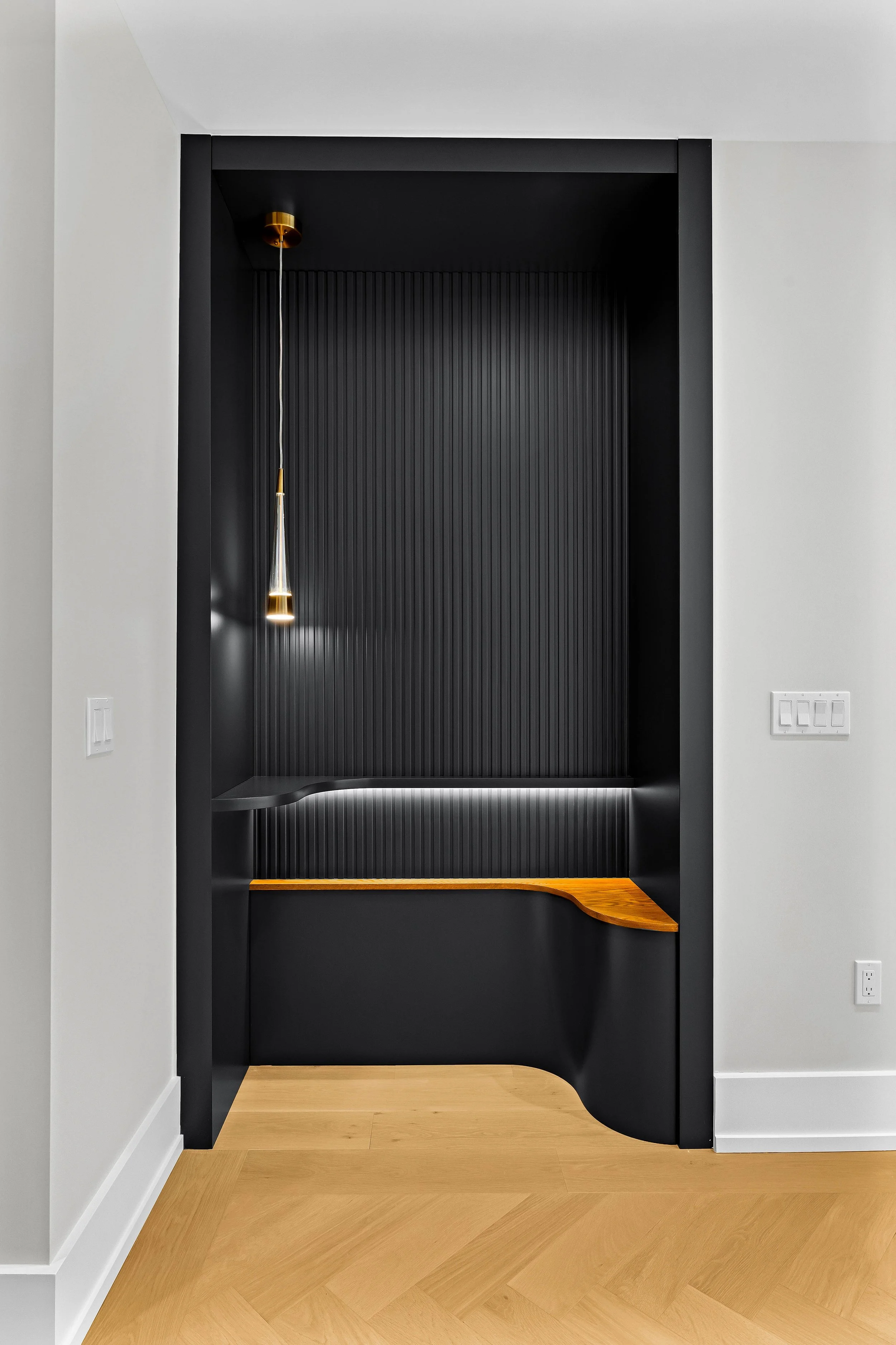 Modern black and wood nook with a hanging pendant light, built-in bench, and textured back wall.