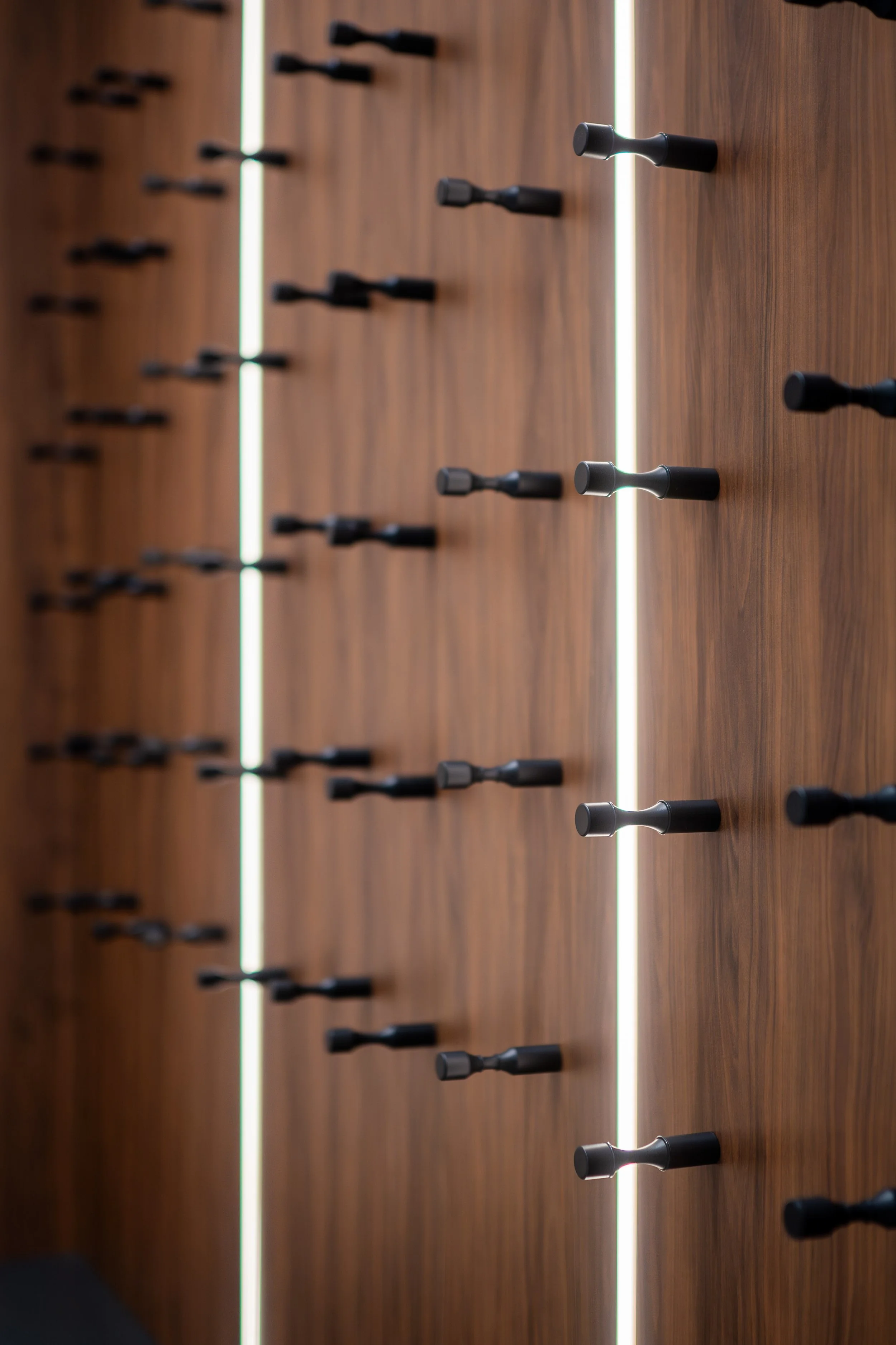 Close-up of a wooden wall with black pegs in a grid pattern and vertical LED light strips.