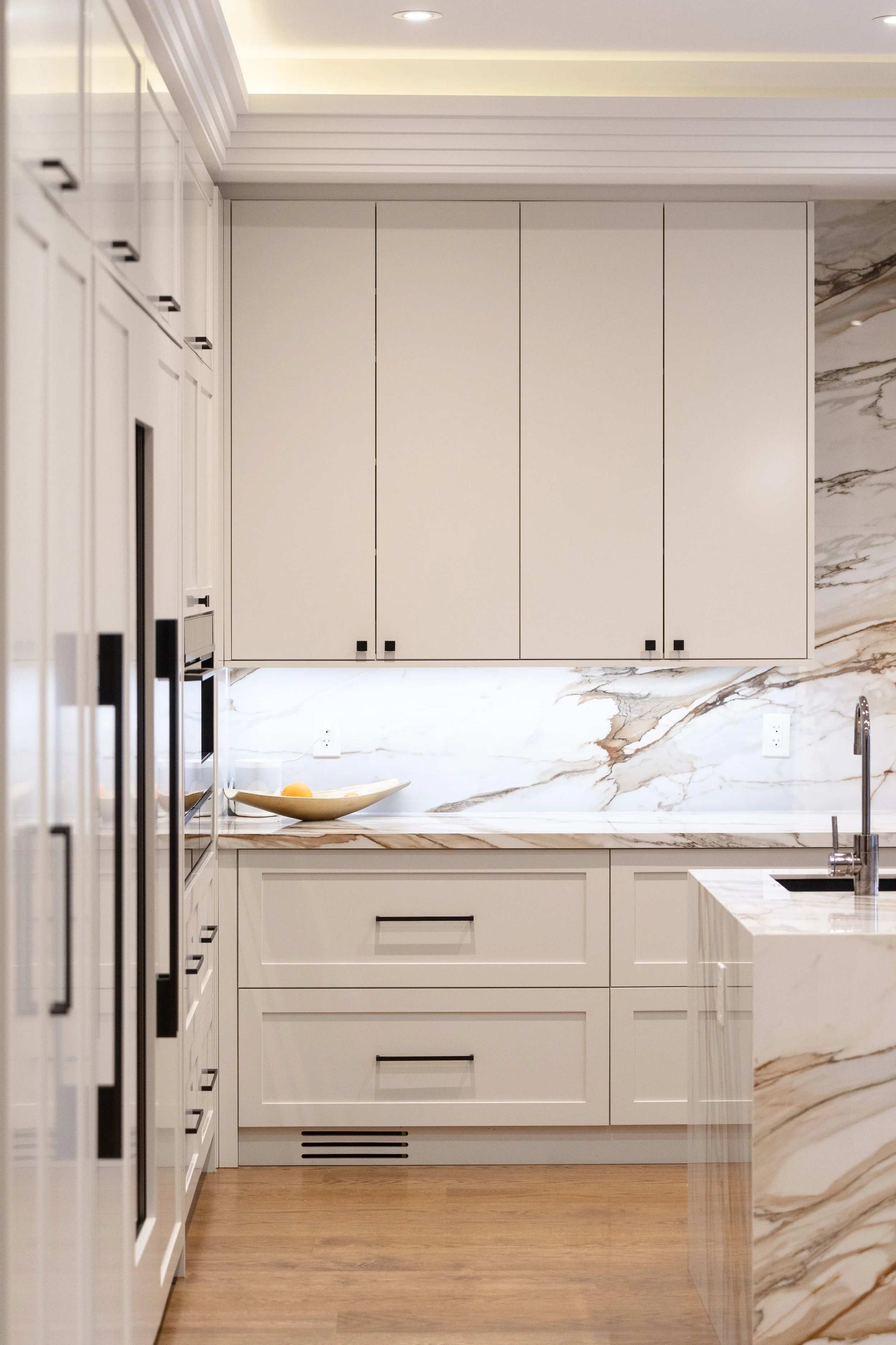 Modern kitchen with white cabinets, marble countertops and backsplash, and a built-in oven and microwave.