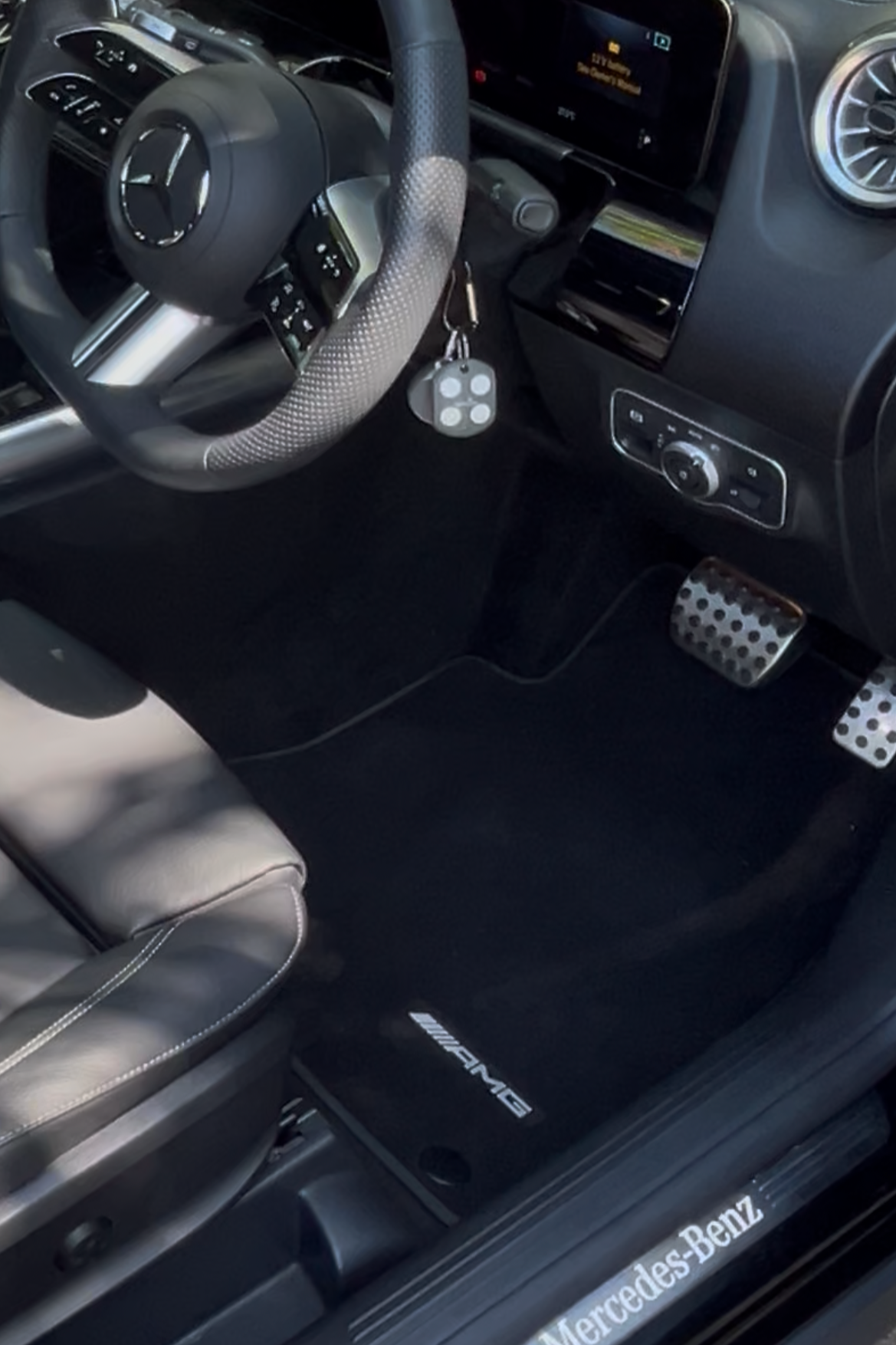 Interior of a Mercedes-Benz AMG vehicle with black carpet, leather seat, and Yamaha heel-toe pedal set, including racing-style accelerator and brake pedals.