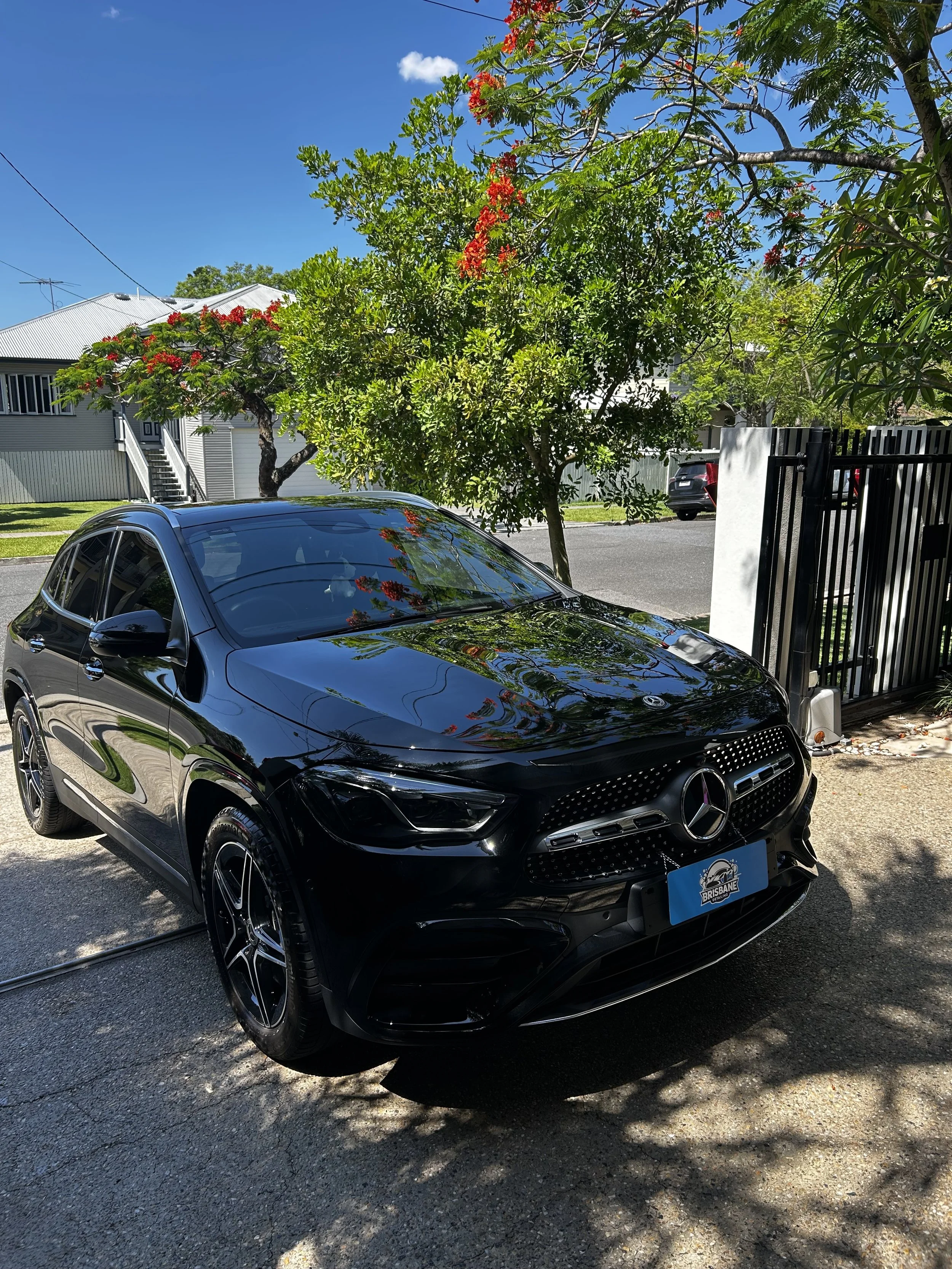 A black Mercedes-Benz parked in a residential driveway with trees and houses in the background under a blue sky.