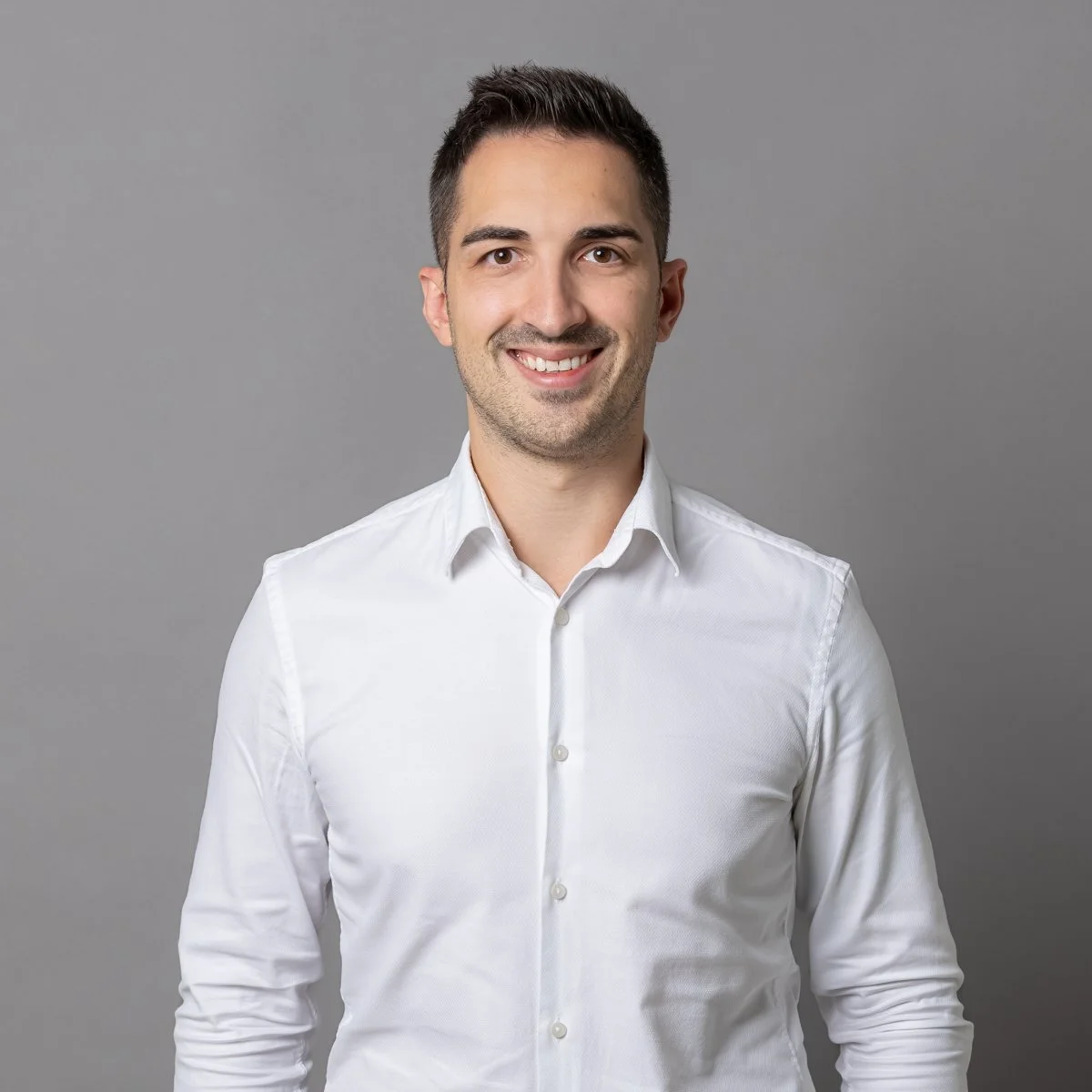 Porträt eines lächelnden Mannes in weißem Hemd vor grauem Hintergrund.