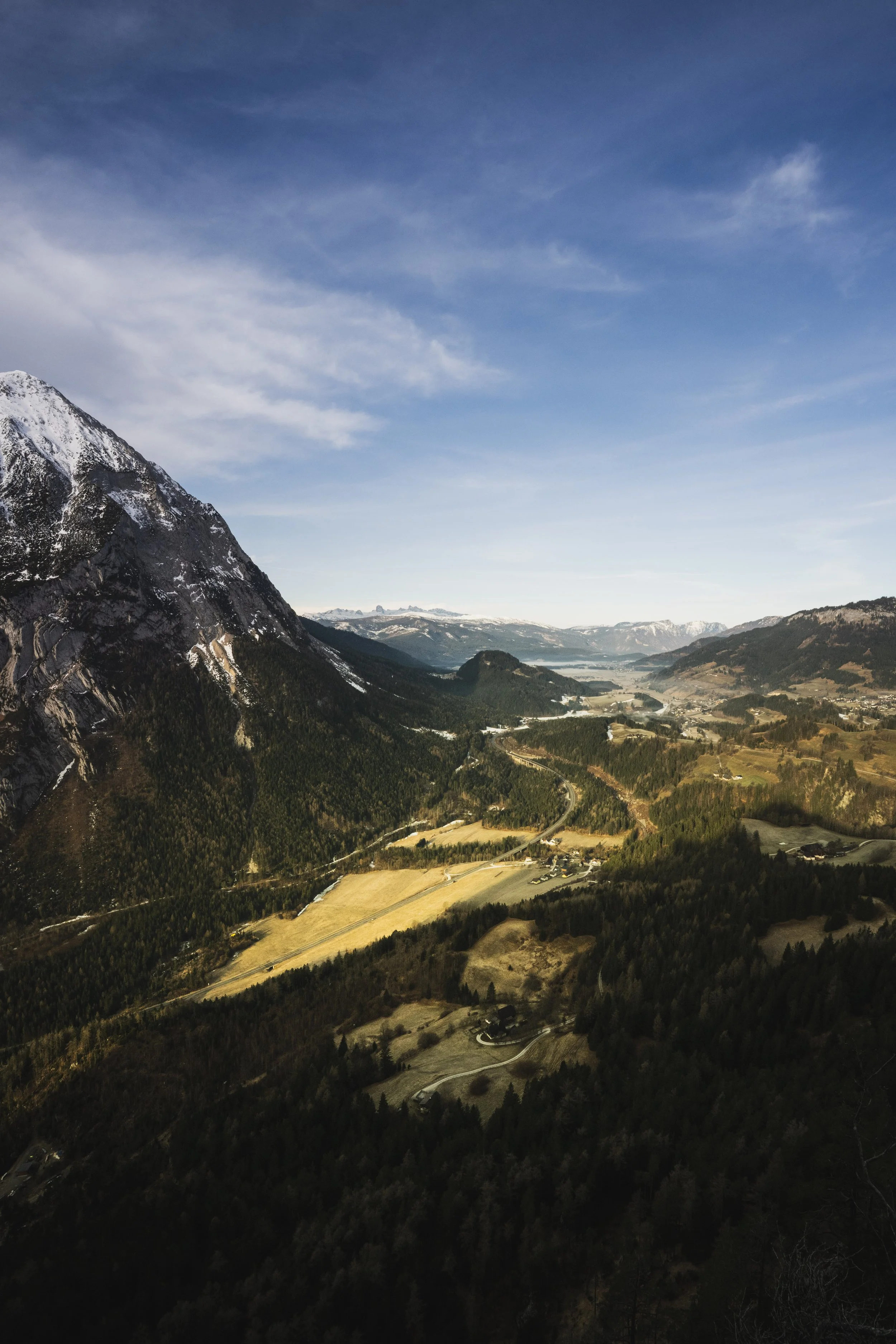 Berglandschaft mit schneebedecktem Gipfel und bewaldeten Tälern unter blauem Himmel.