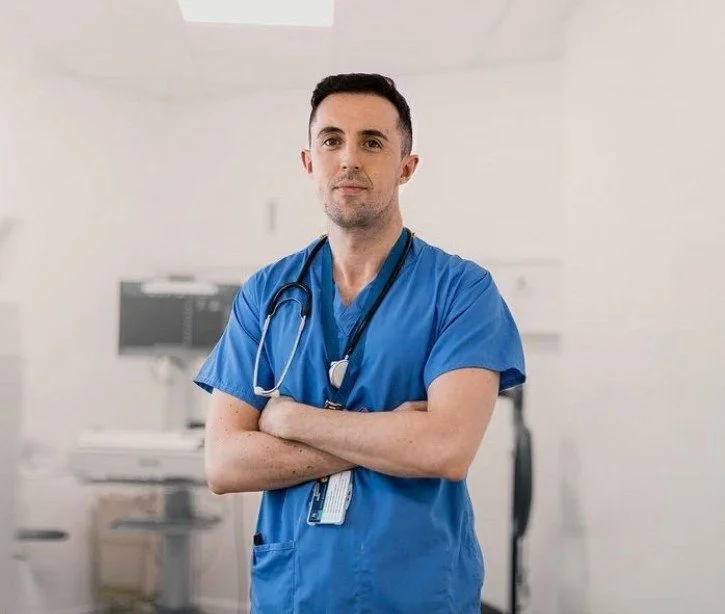 Male doctor in blue scrubs with stethoscope standing in a medical office. Cardiac screening, hi-tech