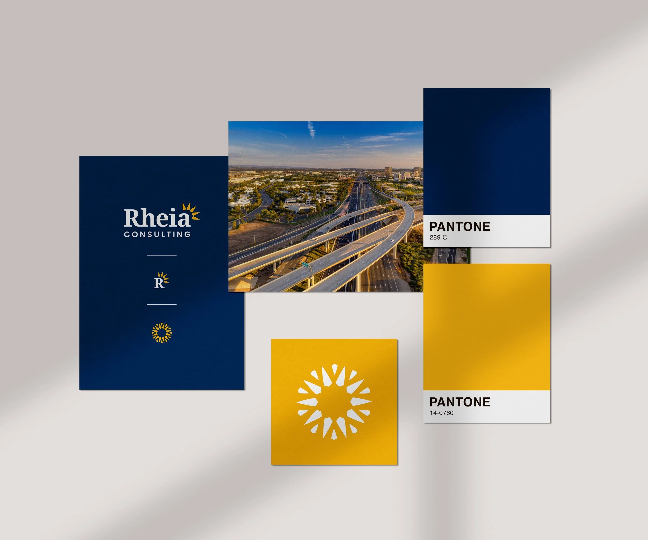 A branding and marketing design layout with a blue, yellow, and white color scheme. It features a cityscape photo of highways and bridges, the company name 'Rheia Consulting', color swatches labeled 'Pantone 289 C' and 'Pantone 14-0760', and the Rheia logo with a sunburst symbol.
