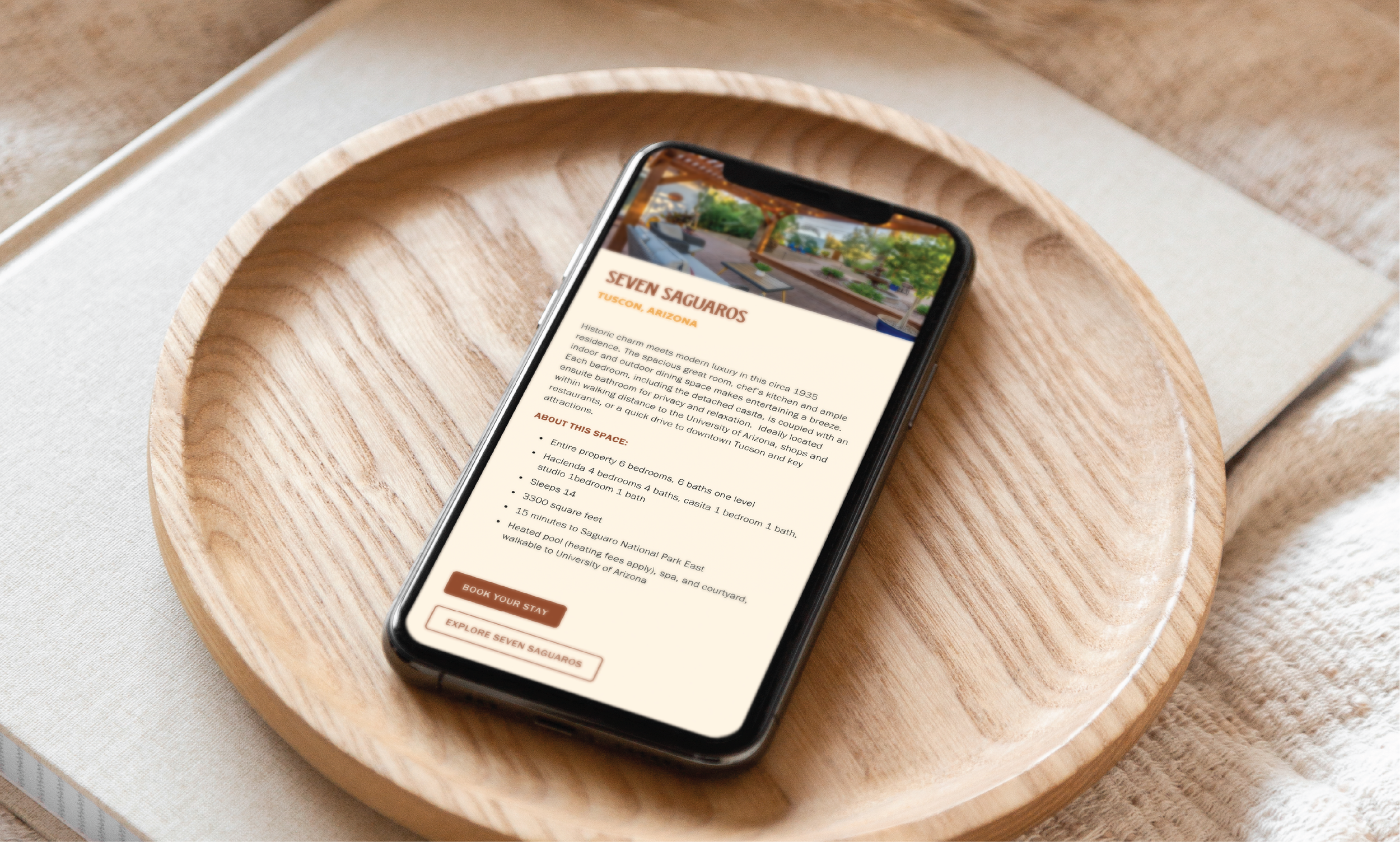 Smartphone on a wooden tray displaying a webpage about Seven Saguaro in Tucson, Arizona, with a header image of an outdoor patio area.