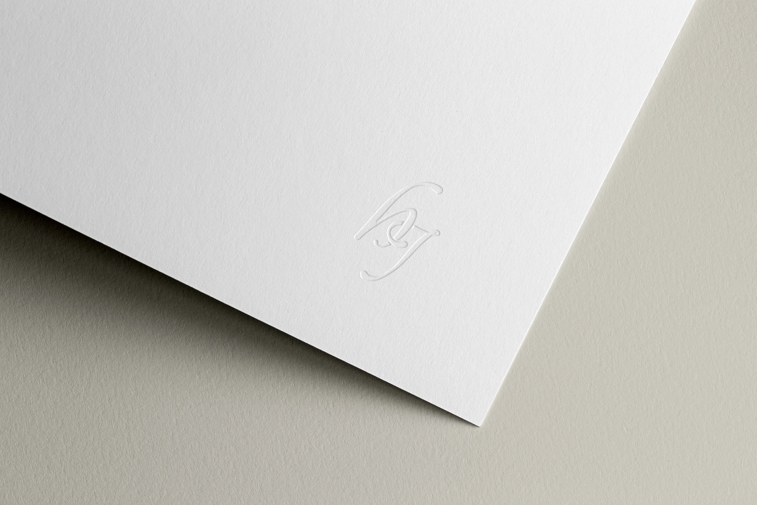 Close-up of a white textured paper with an embossed, stylized monogram or logo near the corner.