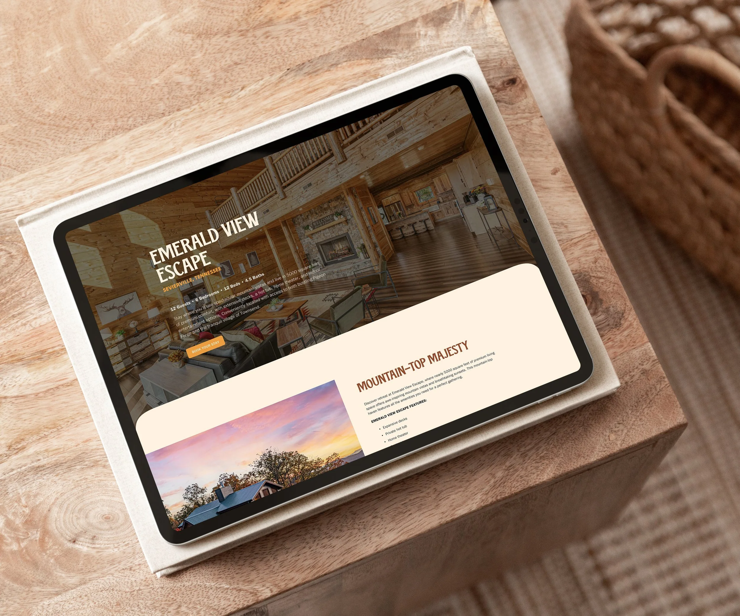 Tablet on a wooden table displaying a webpage for 'Emerald View Escape,' a cabin rental property in Sevierville, Tennessee, featuring interior photos of a log cabin with a cozy living area and a scenic sunset view of a house with a chimney.