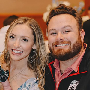 A smiling woman and a smiling man posing together at an indoor event.