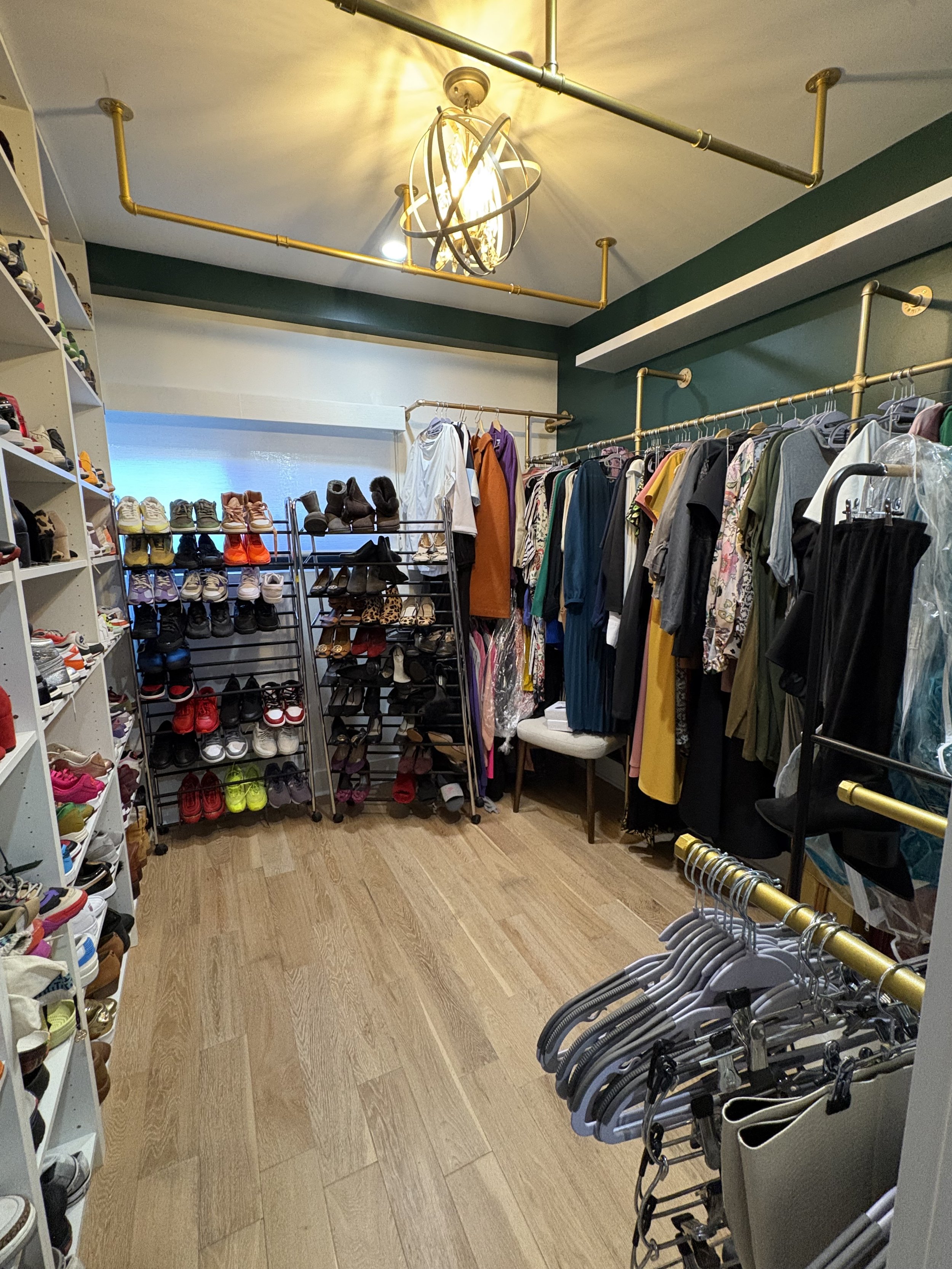 Walk-in closet with hanging clothes, shoe racks filled with various shoes, and a modern light fixture on the ceiling.