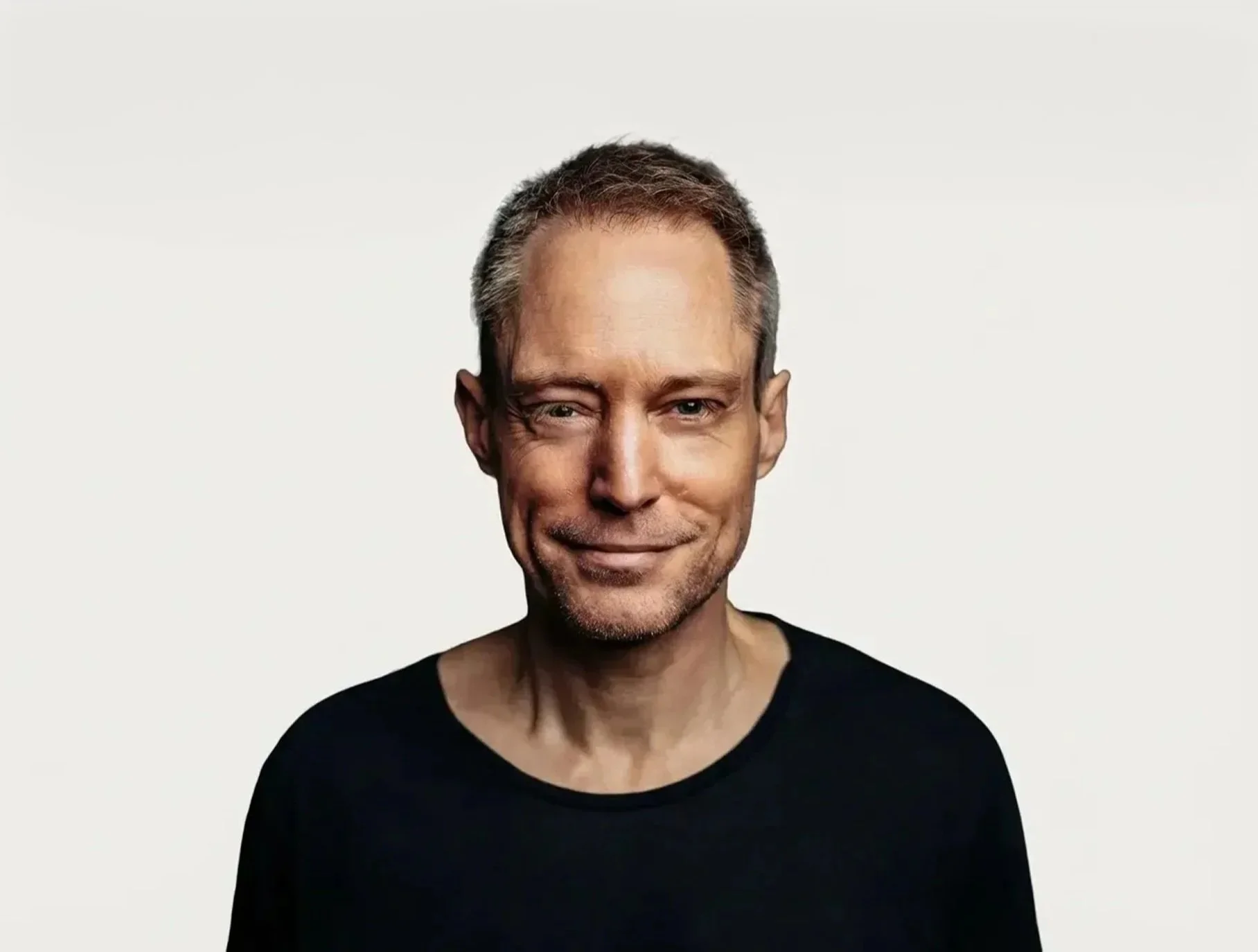 A middle-aged man with short hair and a slight smile, wearing a black shirt, standing against a plain white background.