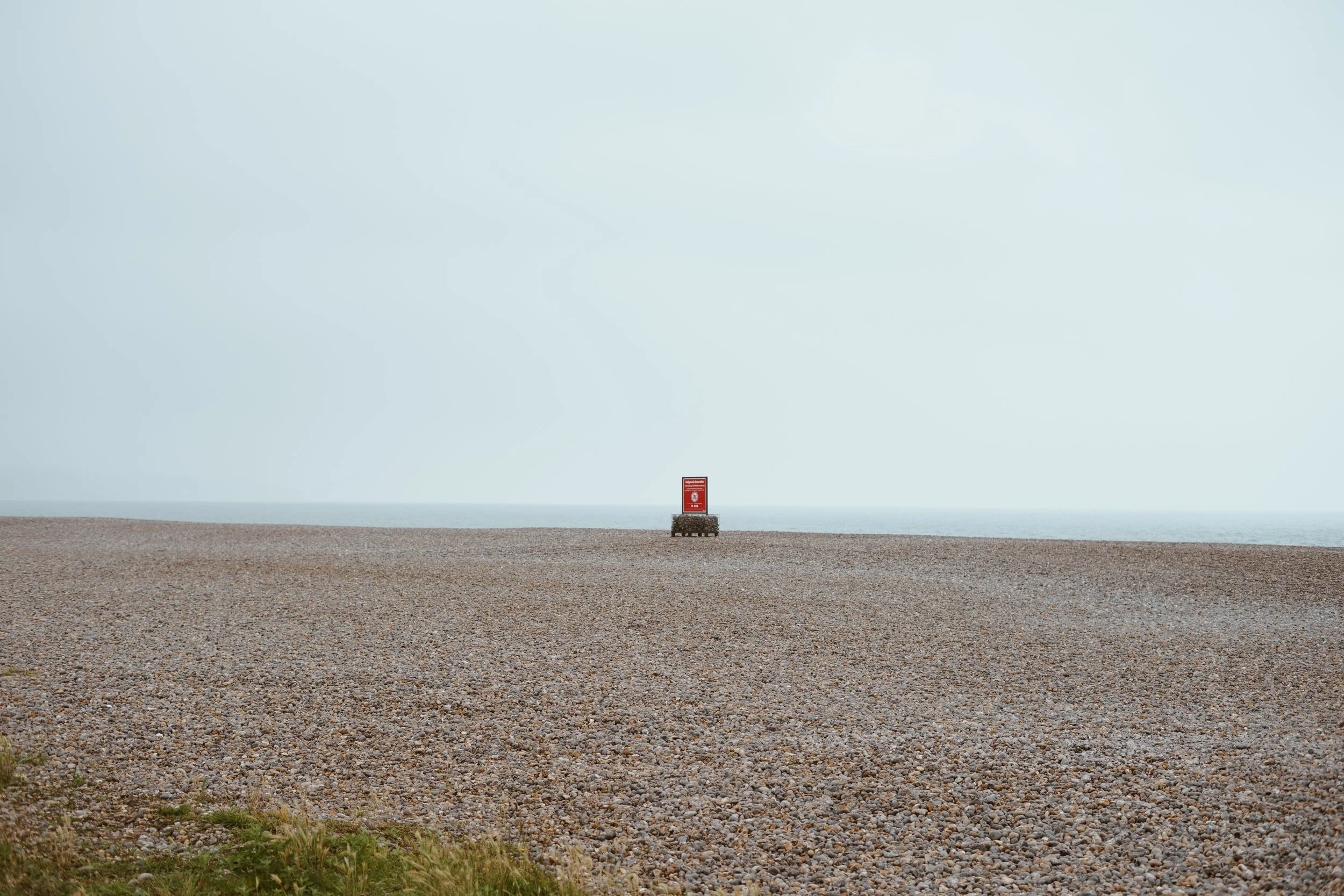 Een leeg strand met een pegelkastje in het midden, onder een bewolkte hemel.