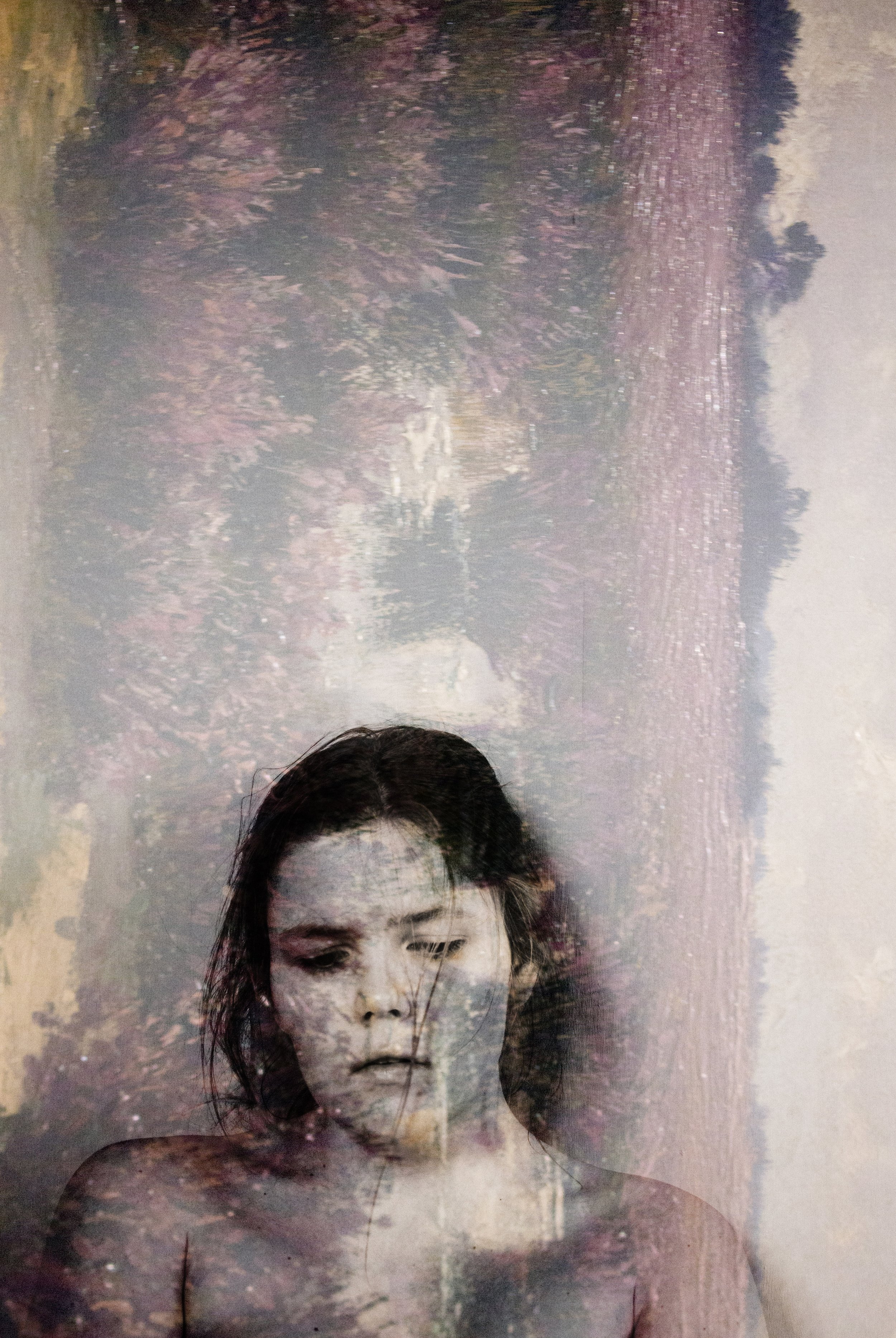 Een dubbelgelaagde compositie met een close-up van een jonge vrouw met nat haar, door een overliggende afbeelding van een landschapselement met bomen en water.