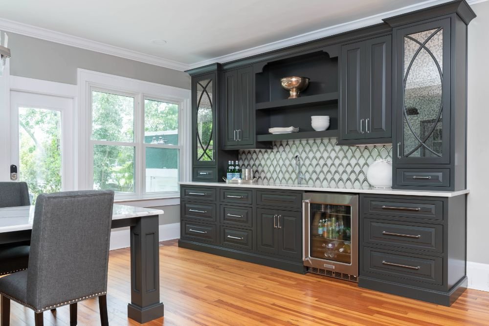 Modern kitchen with dark cabinets, hardwood floor, and dining table. Features tile backsplash, built-in beverage cooler, and large windows.