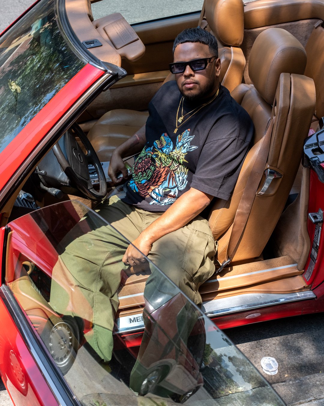 Model reclining in a Mercedes coupe wearing 4-color silkscreen t-shirt featuring original artwork of Cerberus