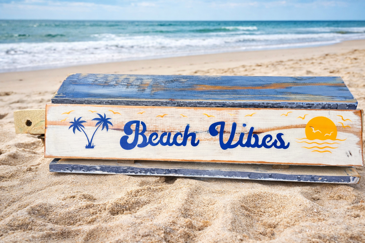a blue and white distressed portable table that rolls up into a bag with the saying Beach Vibes on a sandy beach  rolled up