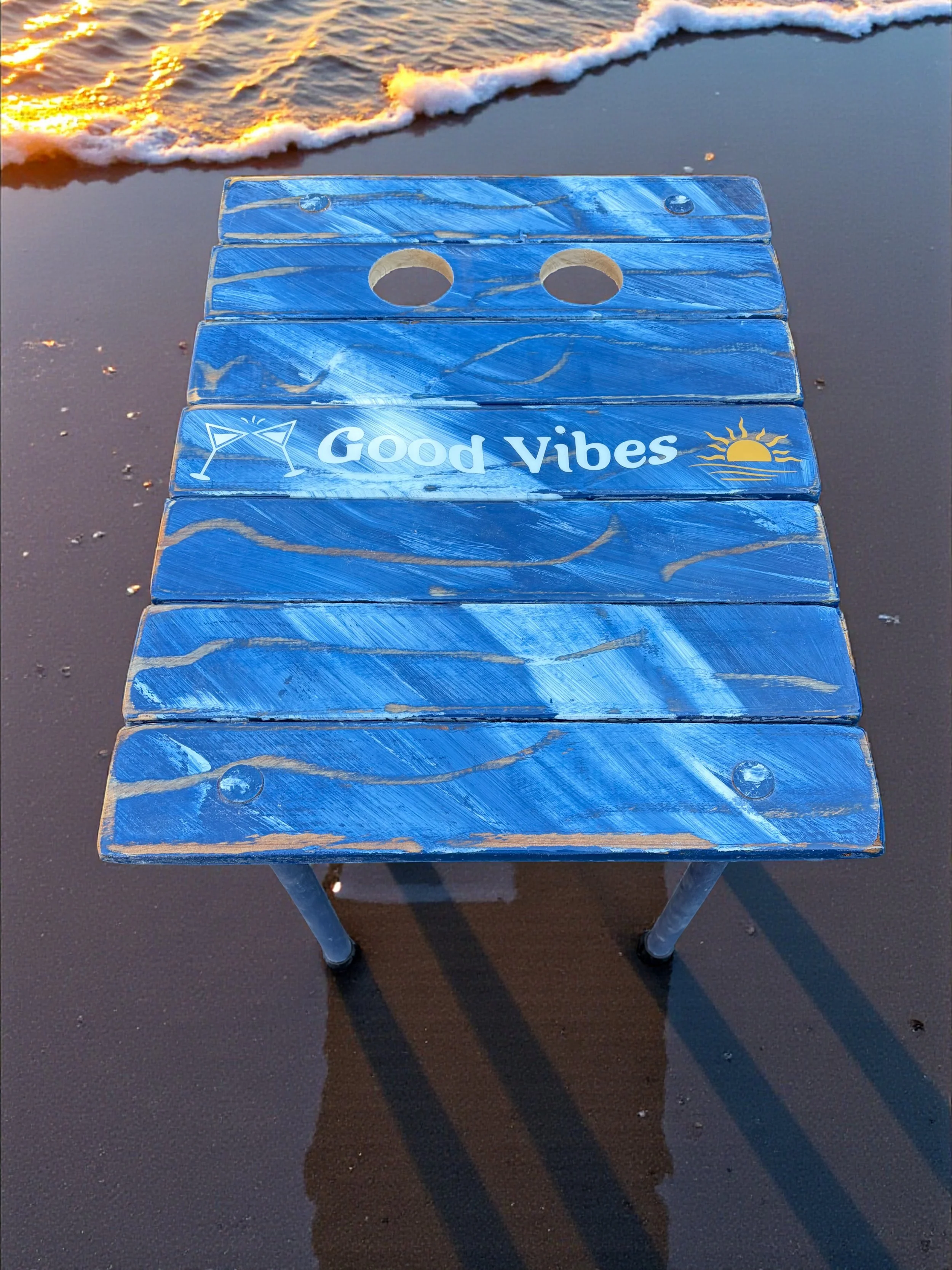 a denim blue good vibes roll up table in a bag on the beach with two cup holders