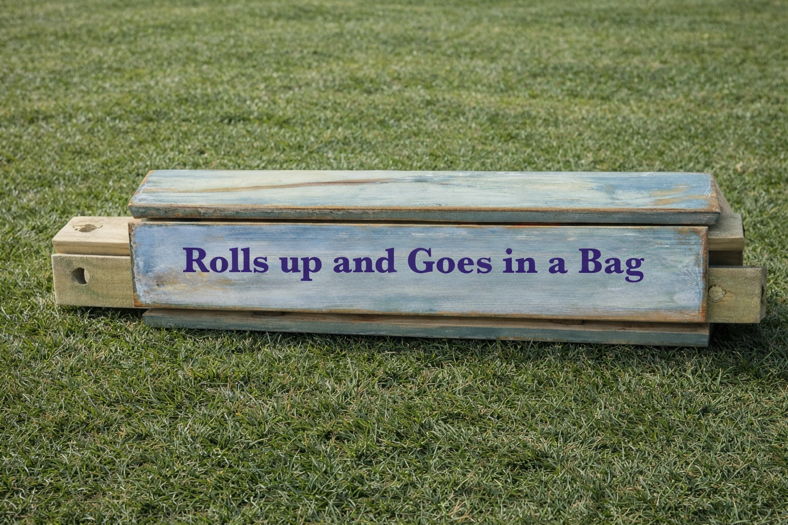 Rolled-up wooden roll-out table on green grass showing compact design that fits into a carrying bag
