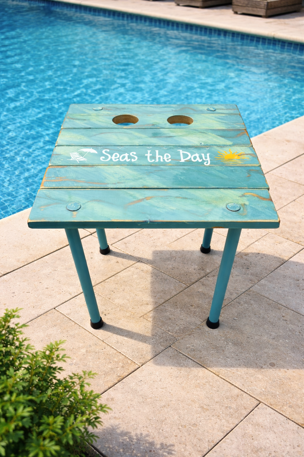 a turquoise beach table that rolls up and says seas the day next to a pool with cup holders
