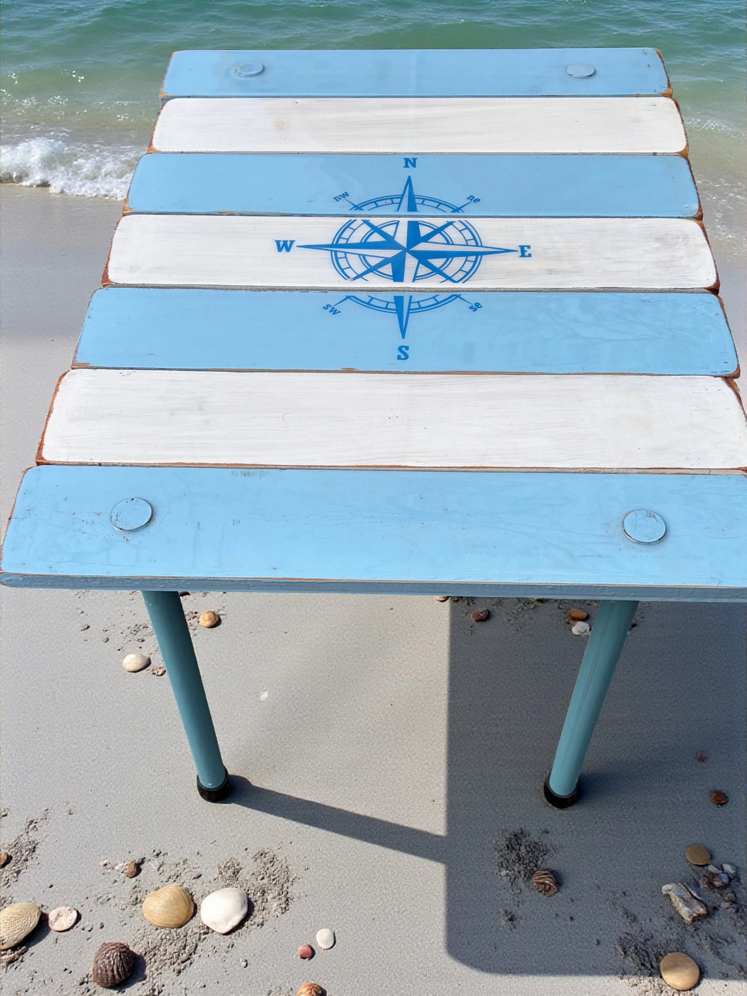 a light blue and white roll out table in a bag with a compass rose on it seen at the beach