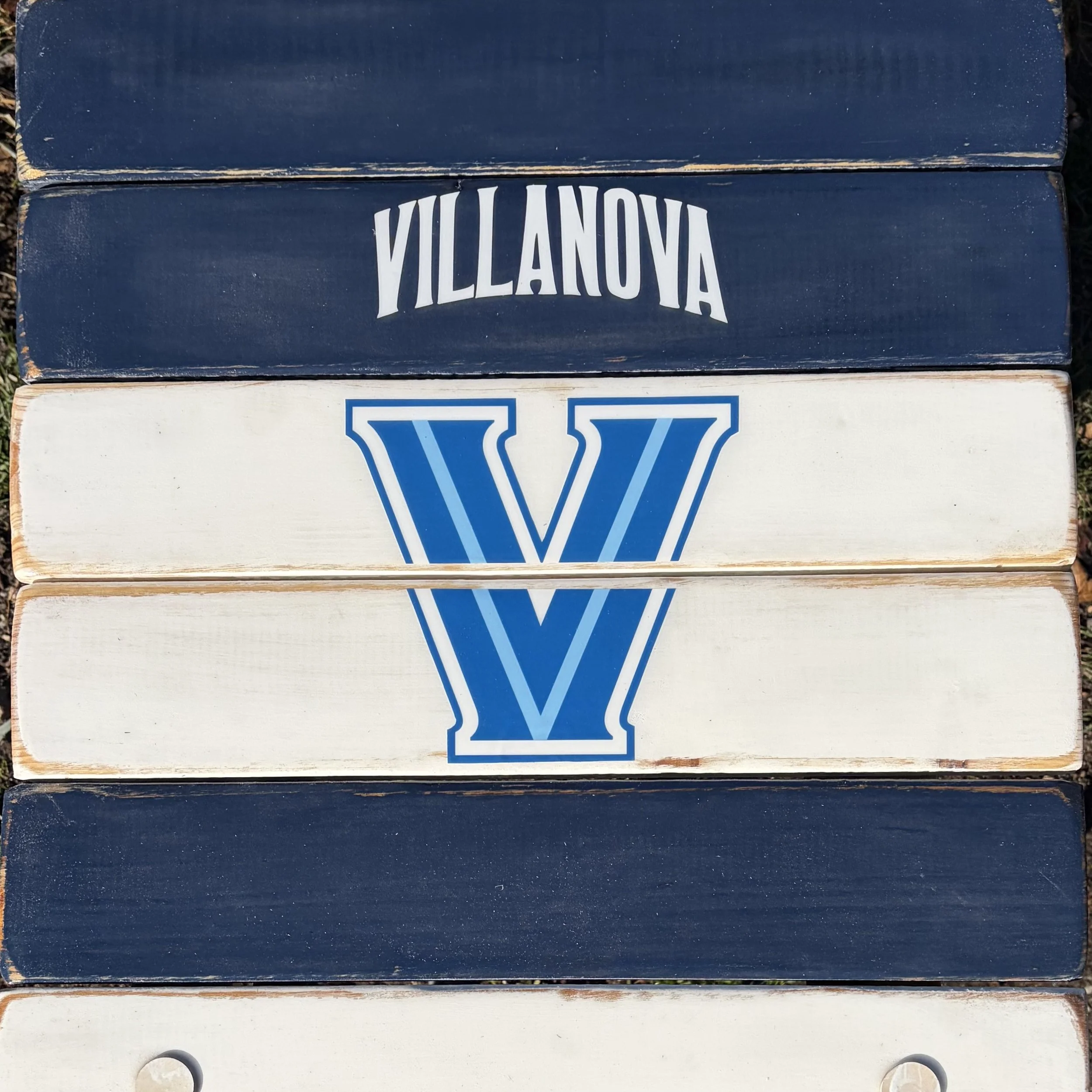 Close-up of Villanova roll-out table logo on handcrafted cedar wood tabletop with navy and white distressed finish