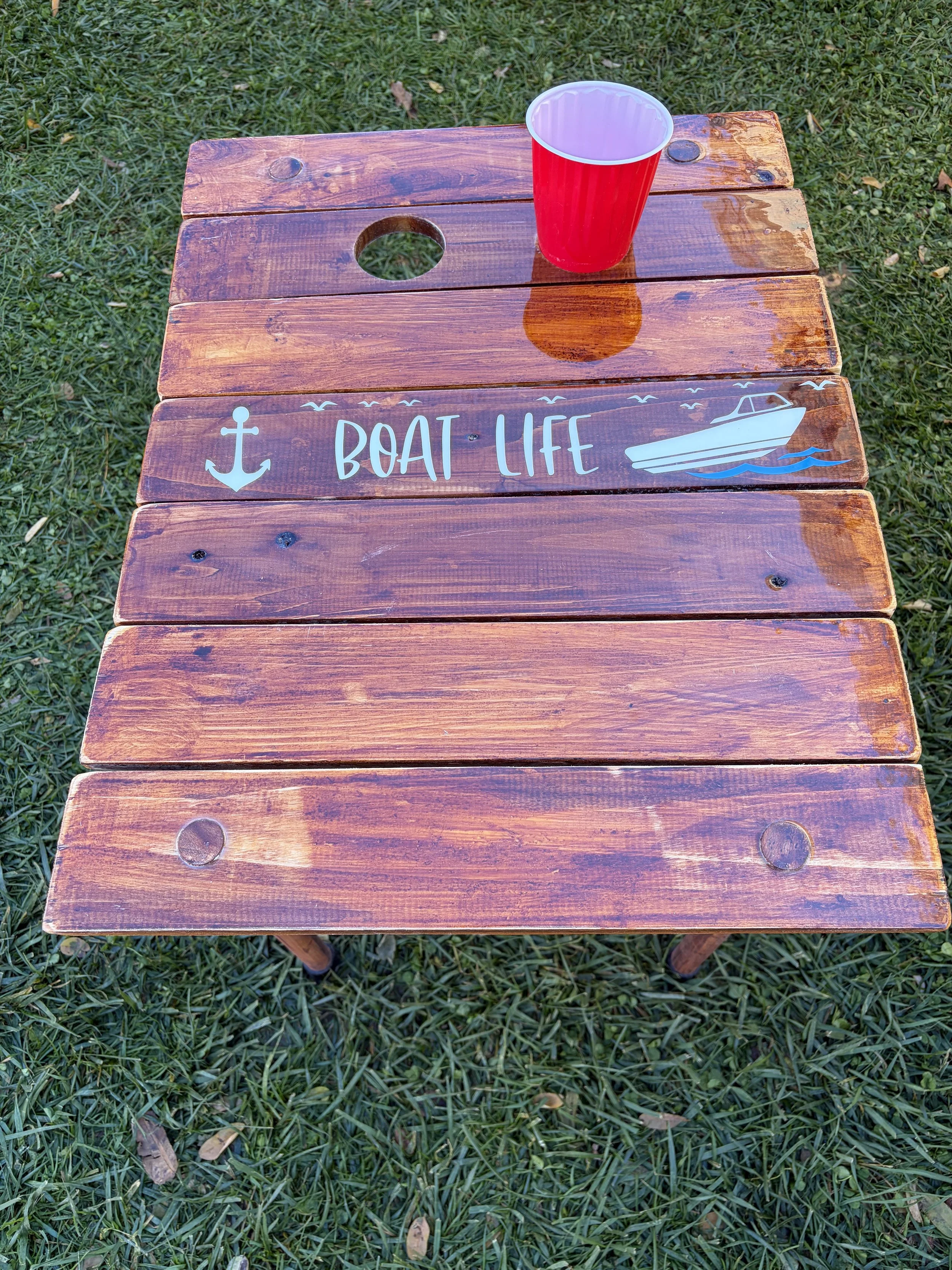 Handcrafted cedar roll-up table on aback yard showing how the holes in the table support red solo cups. it's compact and lightweight outdoor table.