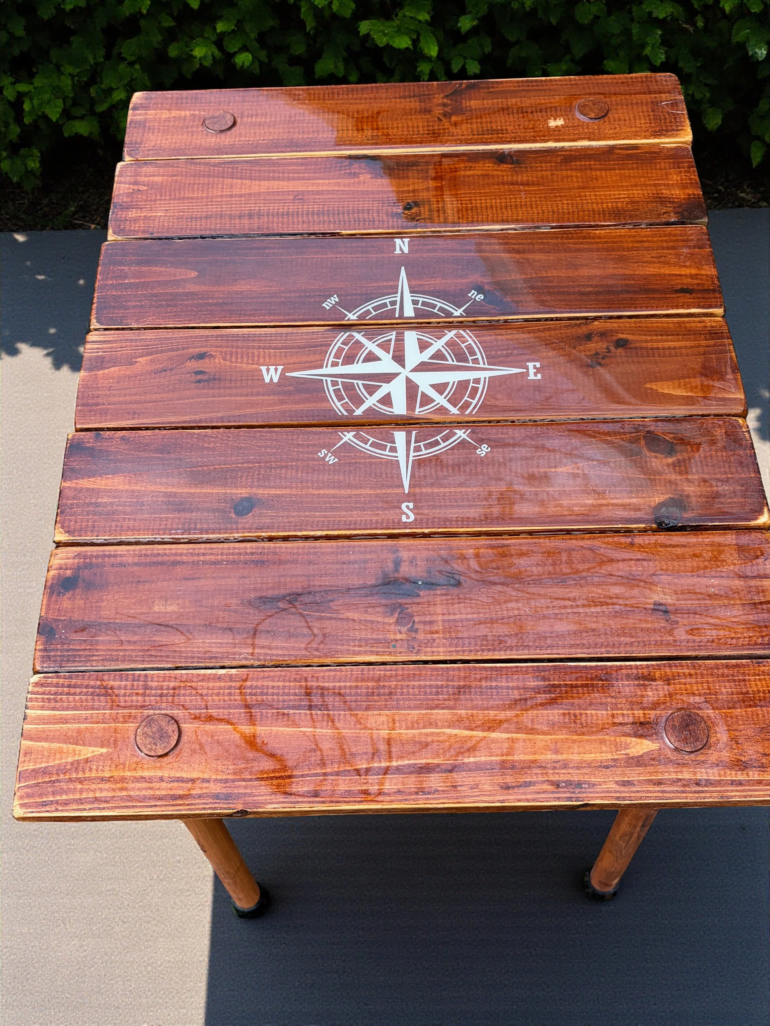 Handcrafted brown compass rose roll-out table in a bag made from cedar wood. Lightweight, portable, and perfect for beach days, boating, camping, tailgates, and outdoor living.