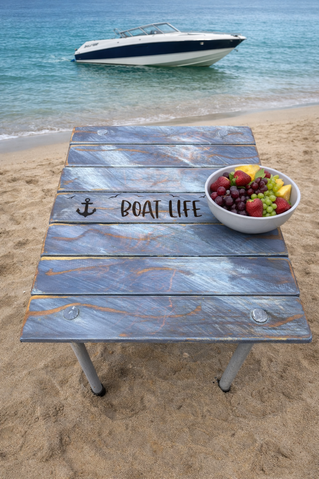 a gray roll up boat table on the beach with a bowl of fruit.