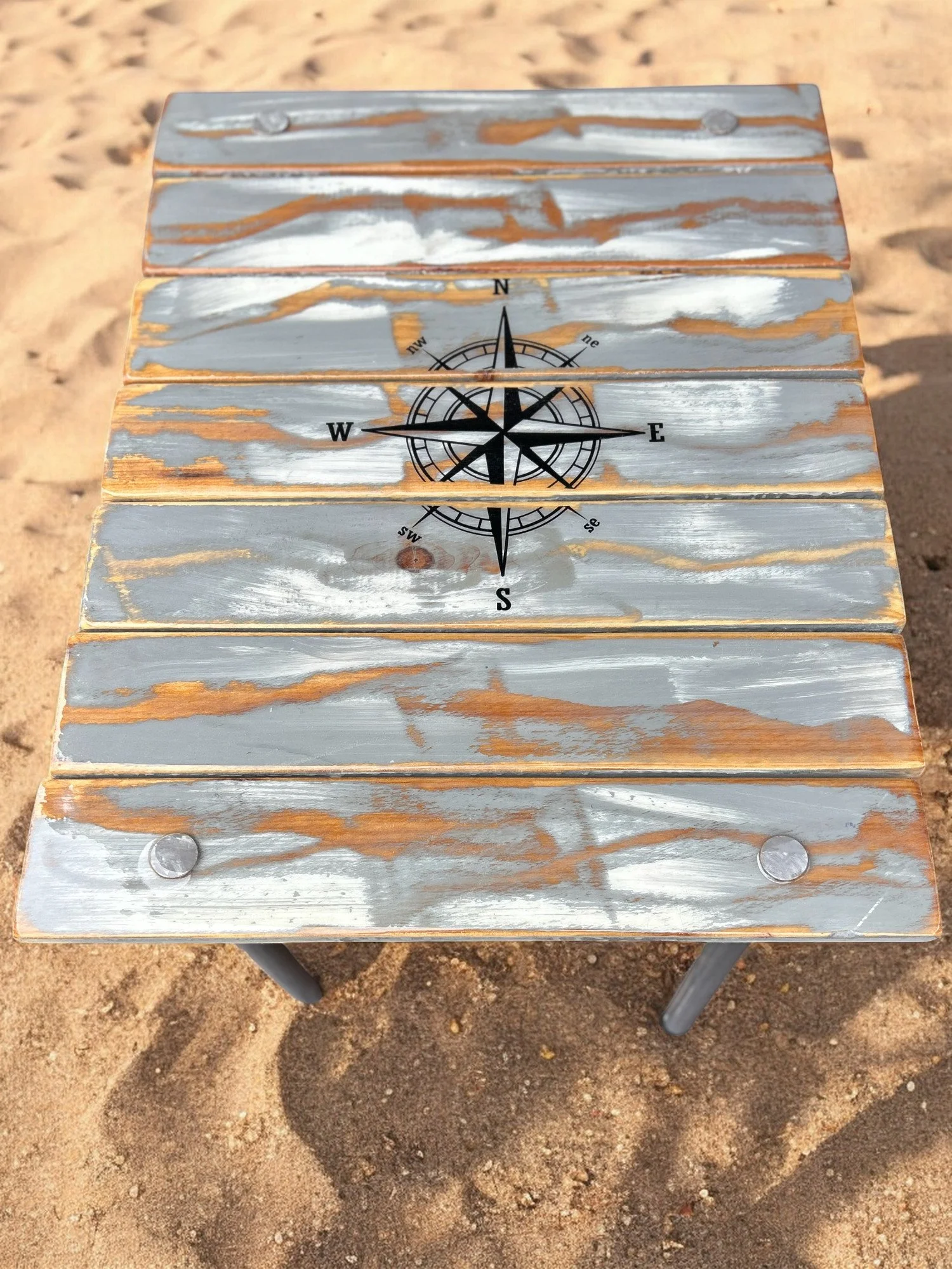 gray whitewashed roll out table in a bag with a black compass rose of it at the beach on a sunny day