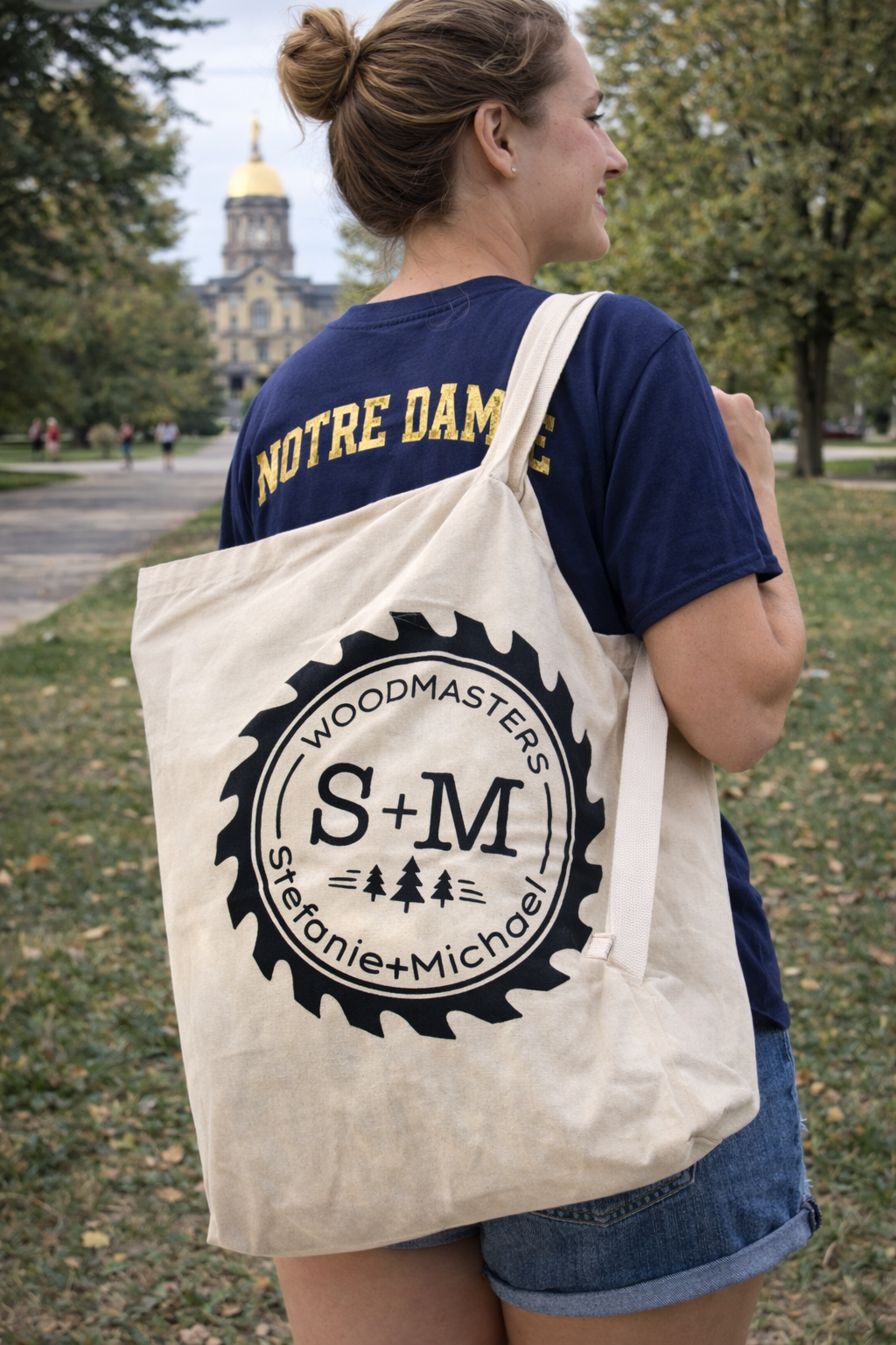 Woodmasters canvas tote bag worn by a female Notre Dame student on campus, natural cotton bag with S+M logo carried over shoulder