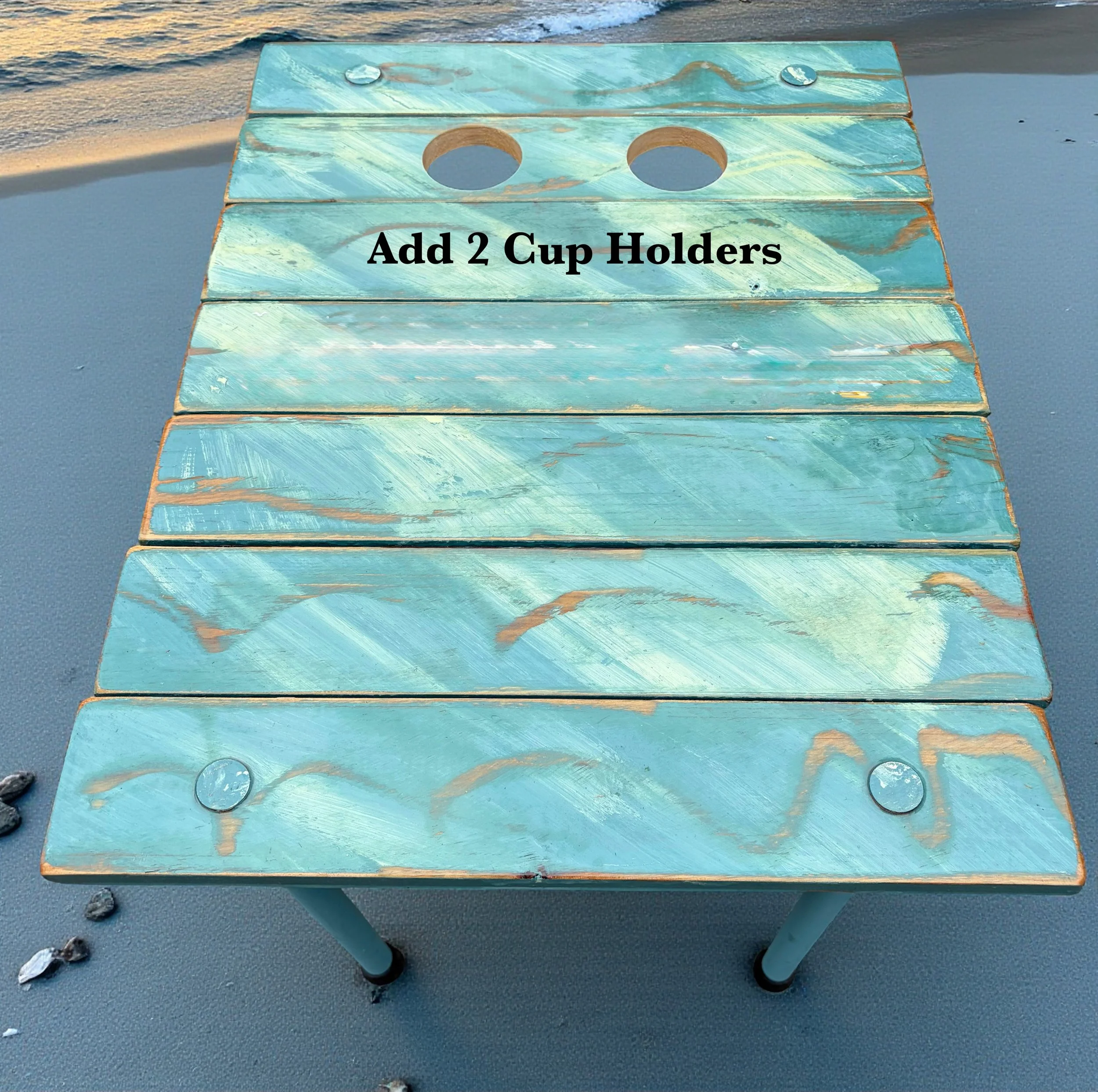 turquoise portable beach table with a white compass rose on the beach with cup holders for red solo cups