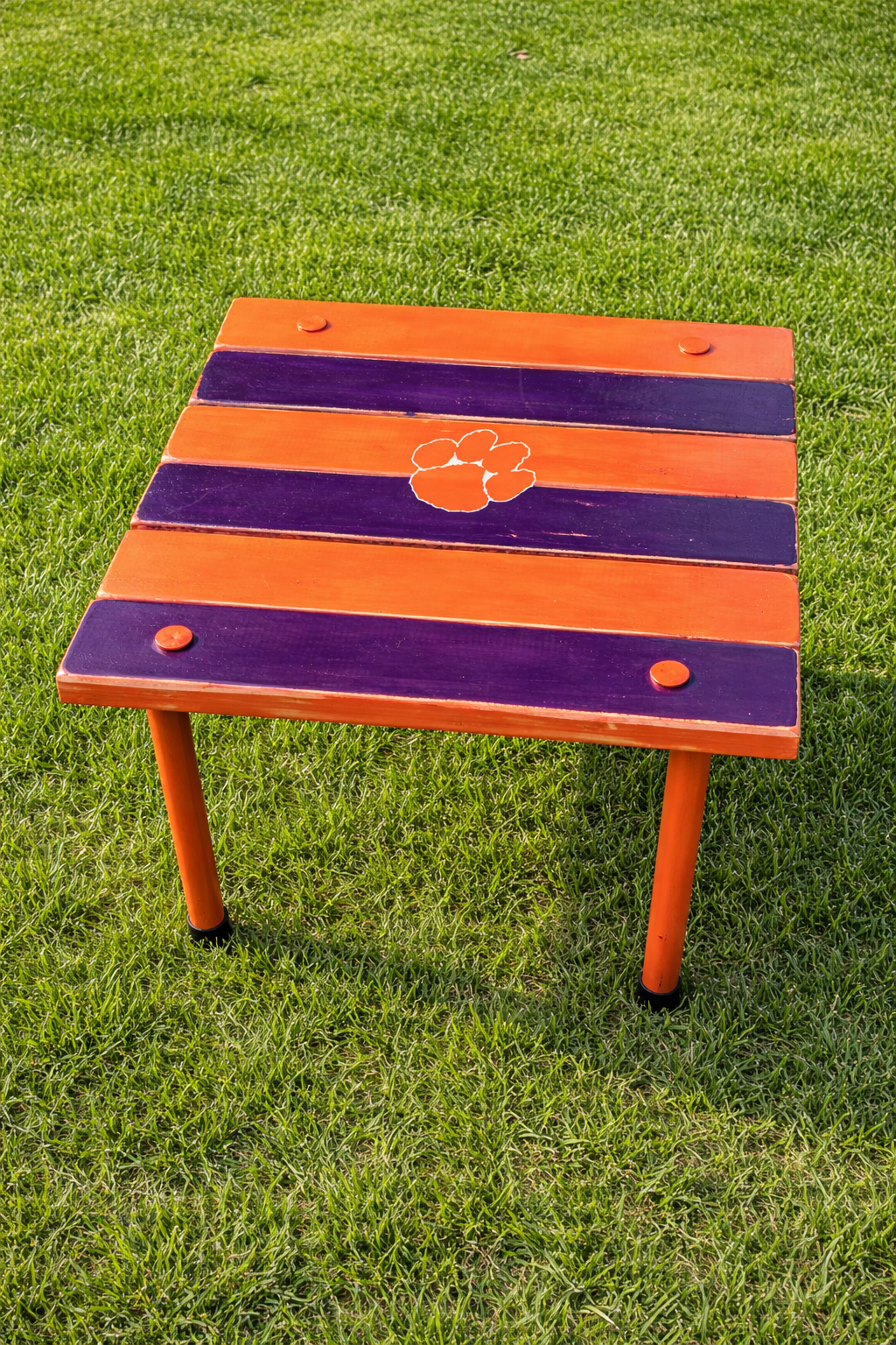 Portable Clemson roll-out table displayed on green grass, handcrafted cedar table in orange and purple with Clemson paw logo