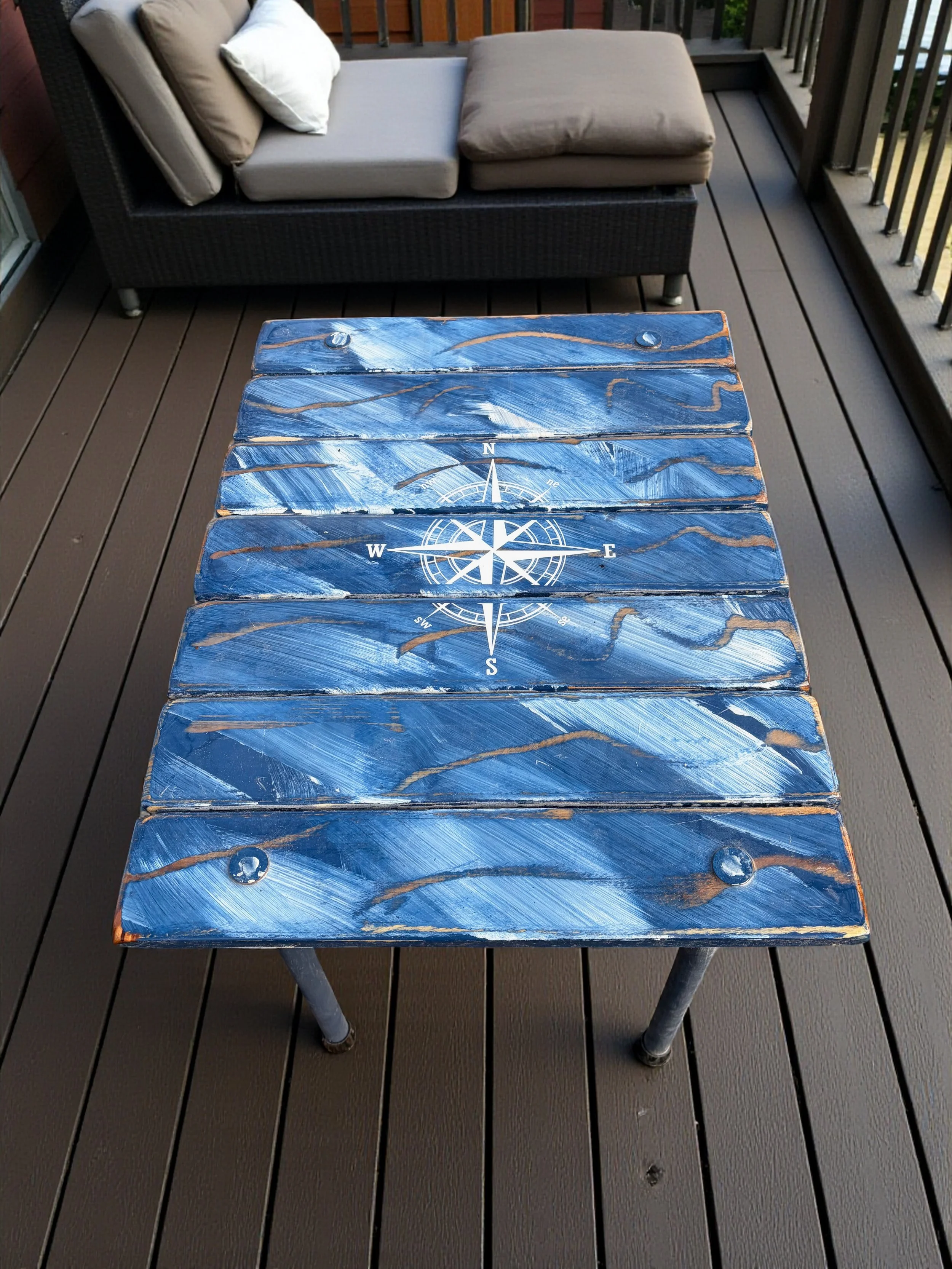 Blue cedar roll-up table with a compass rose design, shown outdoors as a lightweight portable coastal table, on a patio deck