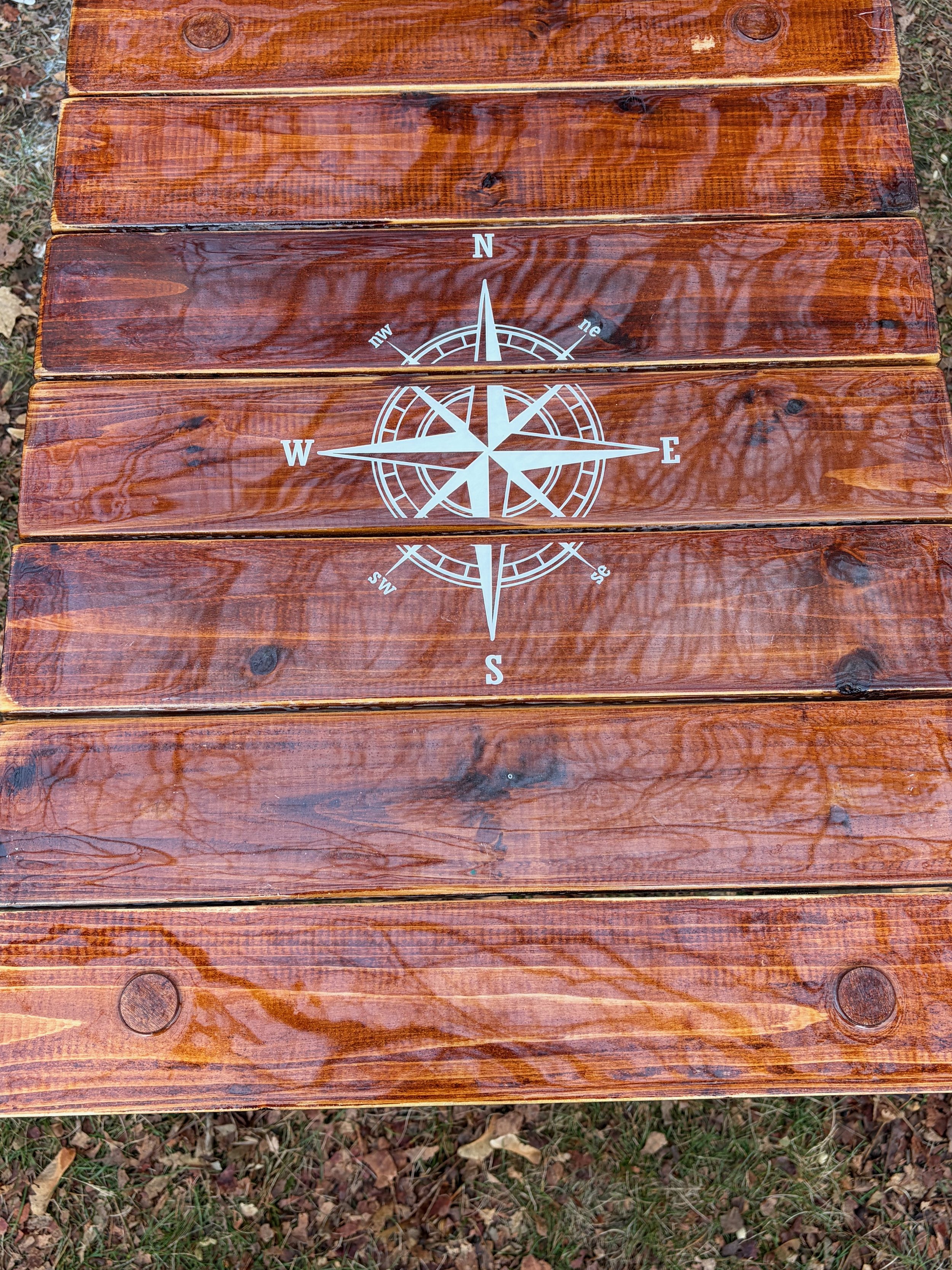 Handcrafted brown compass rose roll-out table in a bag made from cedar wood. Lightweight, portable, and perfect for beach days, boating, camping, tailgates, and outdoor living. a close up view