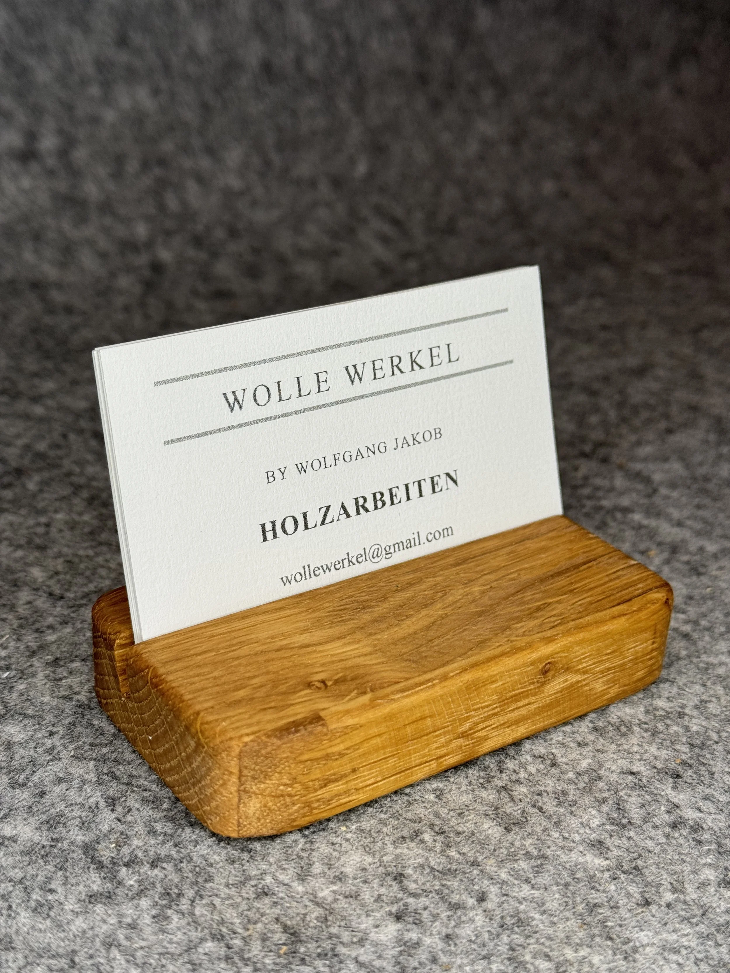 Visitenkarte von Wolle Werkel, platziert in einem Holzhalter auf grauem Hintergrund.